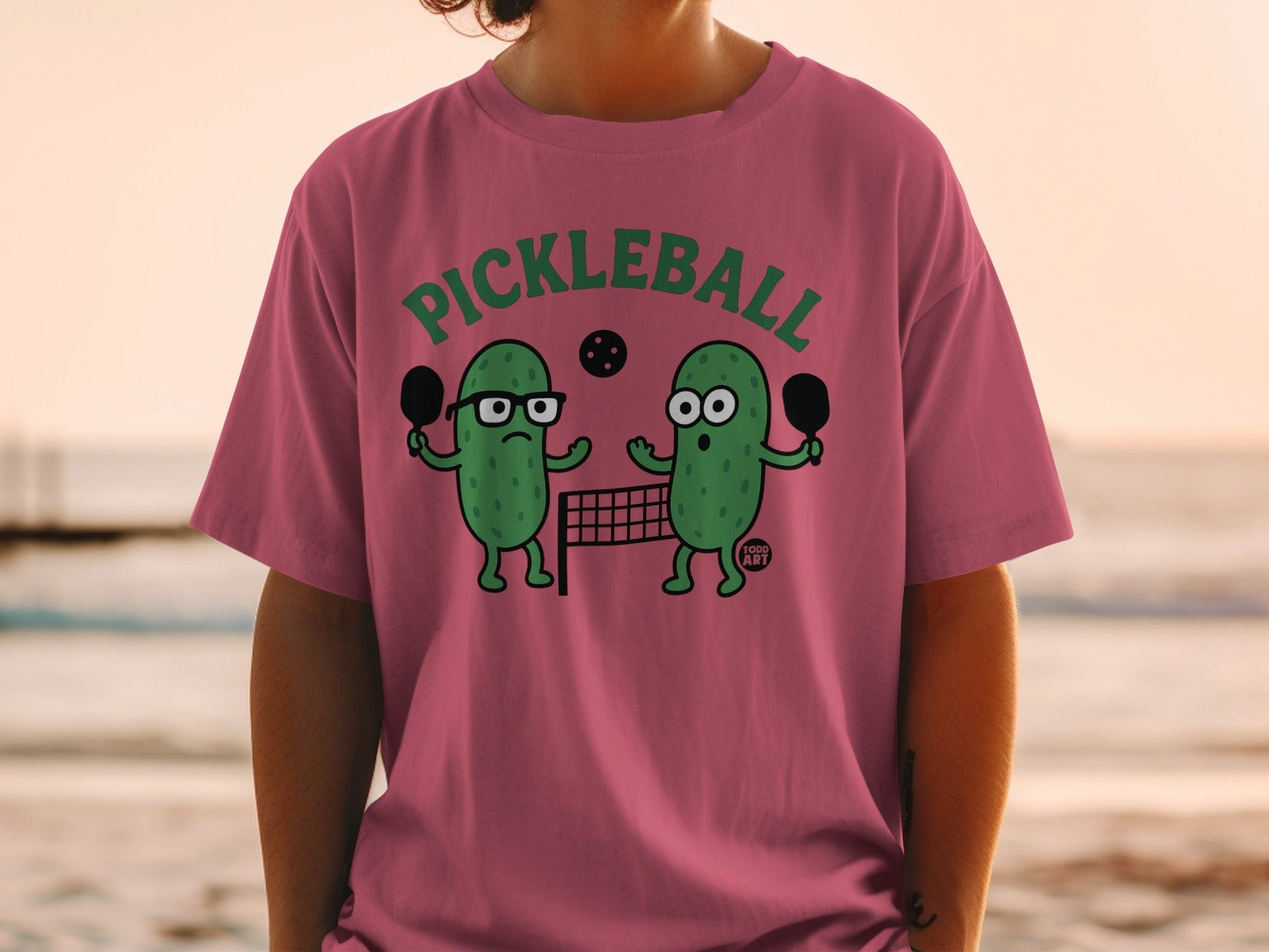 Cartoon pickle characters playing pickleball on a t-shirt.