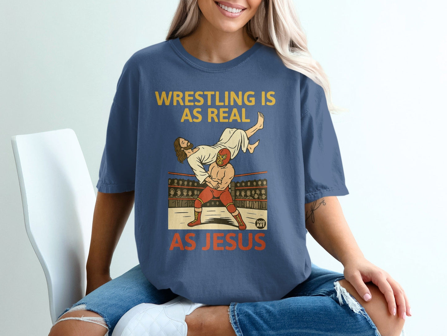 Jesus body slams an opponent in a wrestling ring on a blue t-shirt.