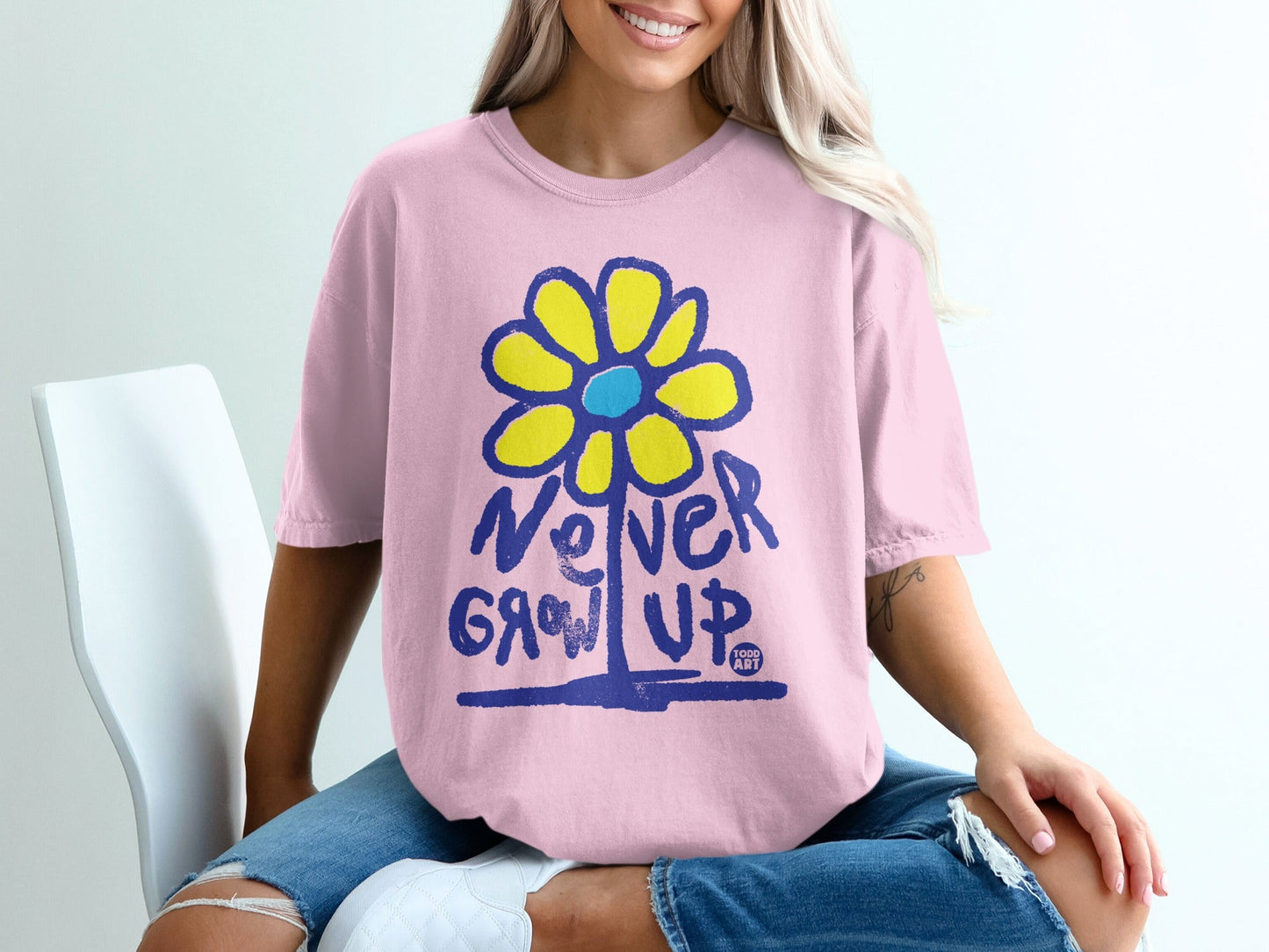 Pink t-shirt with "Never Grow Up" and a yellow and blue flower graphic.