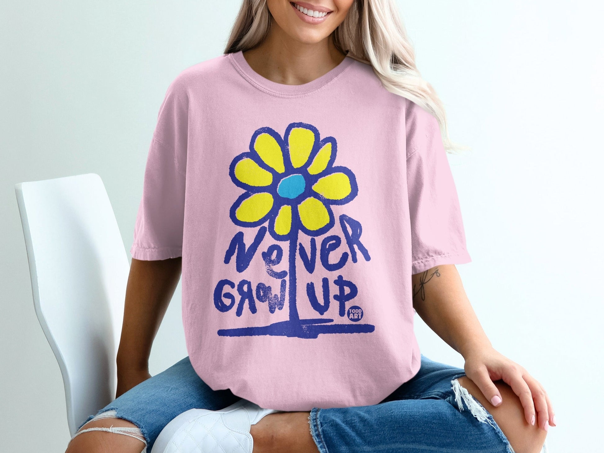 Pink t-shirt with "Never Grow Up" and a yellow and blue flower graphic.