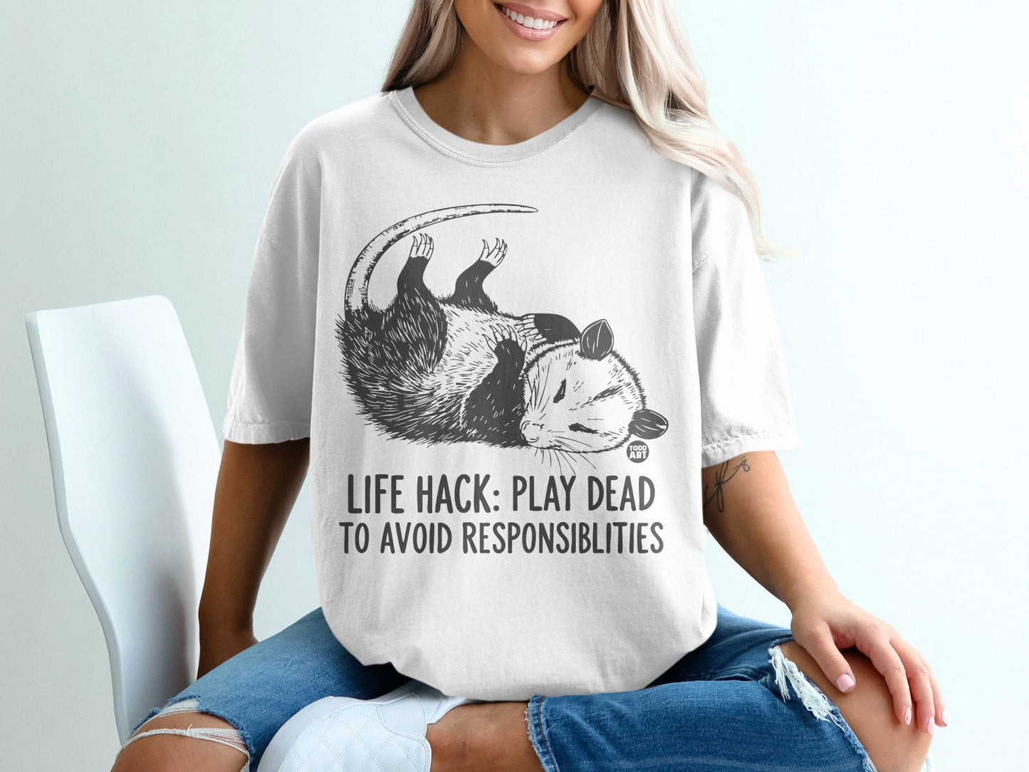 Opossum wearing shirt with text "LIFE HACK: PLAY DEAD TO AVOID RESPONSIBILITIES".
