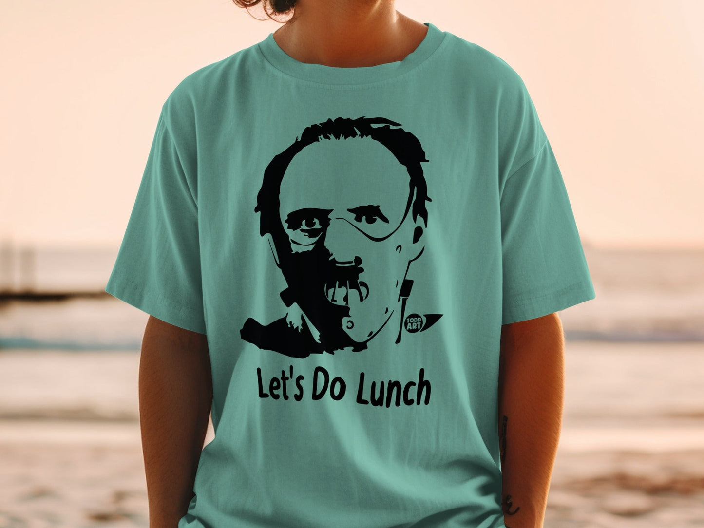 Teal t-shirt with black graphic of Hannibal Lecter and "Let's Do Lunch".