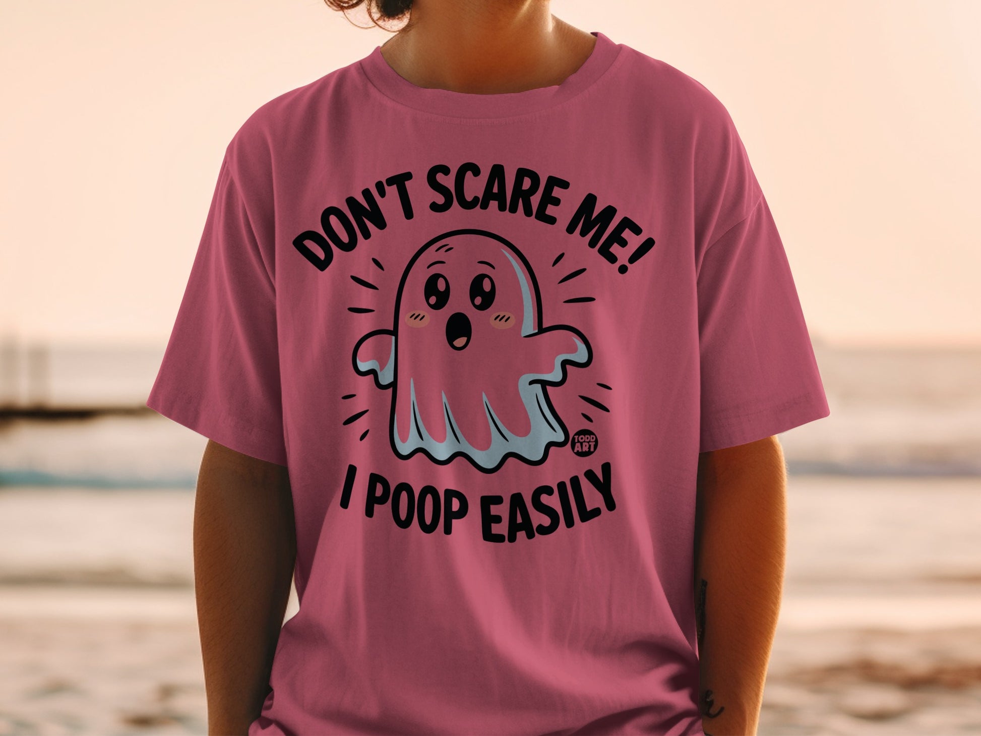 Pink t-shirt with a cartoon ghost saying "Don't scare me! I poop easily."