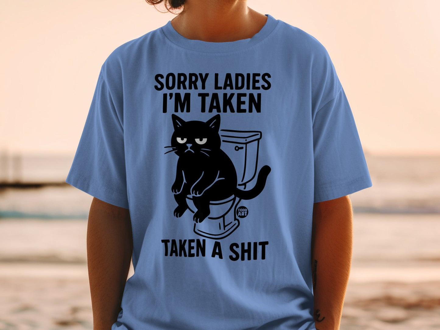 Blue t-shirt with black graphic of a grumpy cat on a toilet, text "SORRY LADIES I'M TAKEN TAKEN A SHIT".
