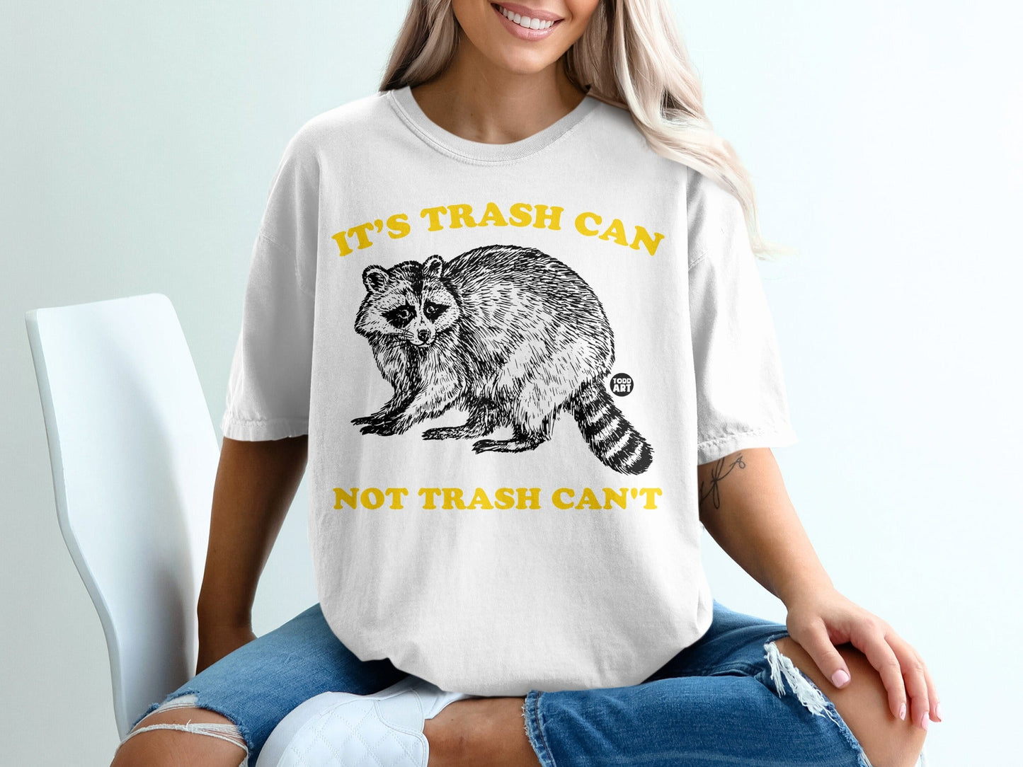 White t-shirt with raccoon graphic and "It's Trash Can Not Trash Can't" text.