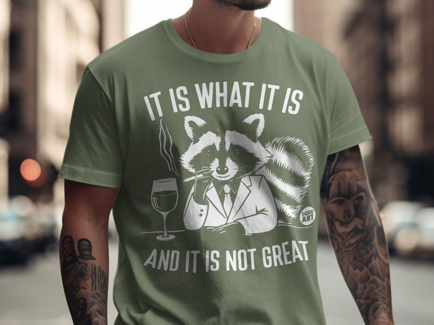 Raccoon in suit smoking, holding wine, on olive green shirt: "It is what it is and it is not great."