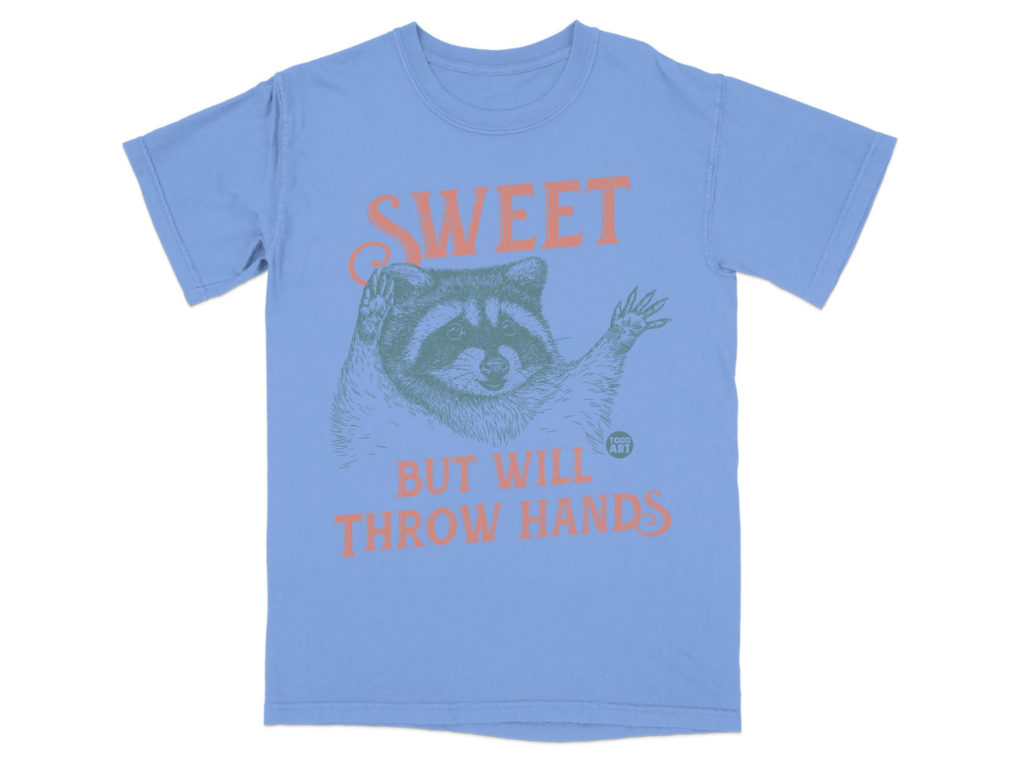 Blue t-shirt with raccoon illustration and text "SWEET BUT WILL THROW HANDS."