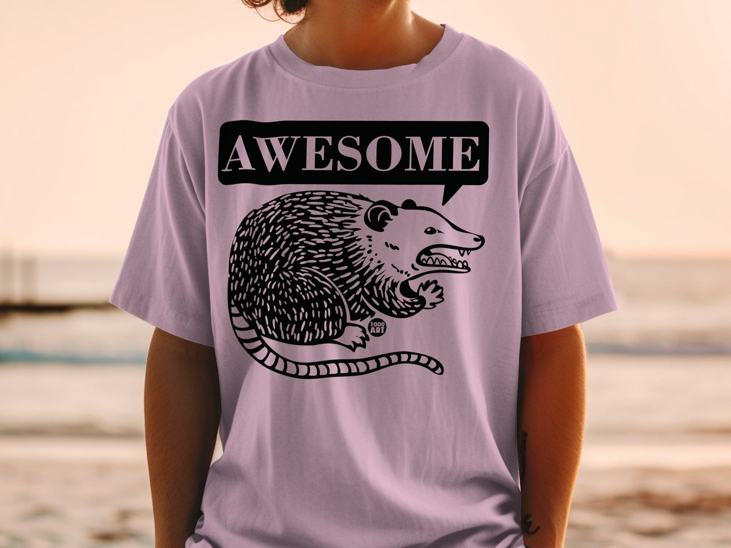 Purple t-shirt with black line drawing of a possum in a speech bubble saying "AWESOME".