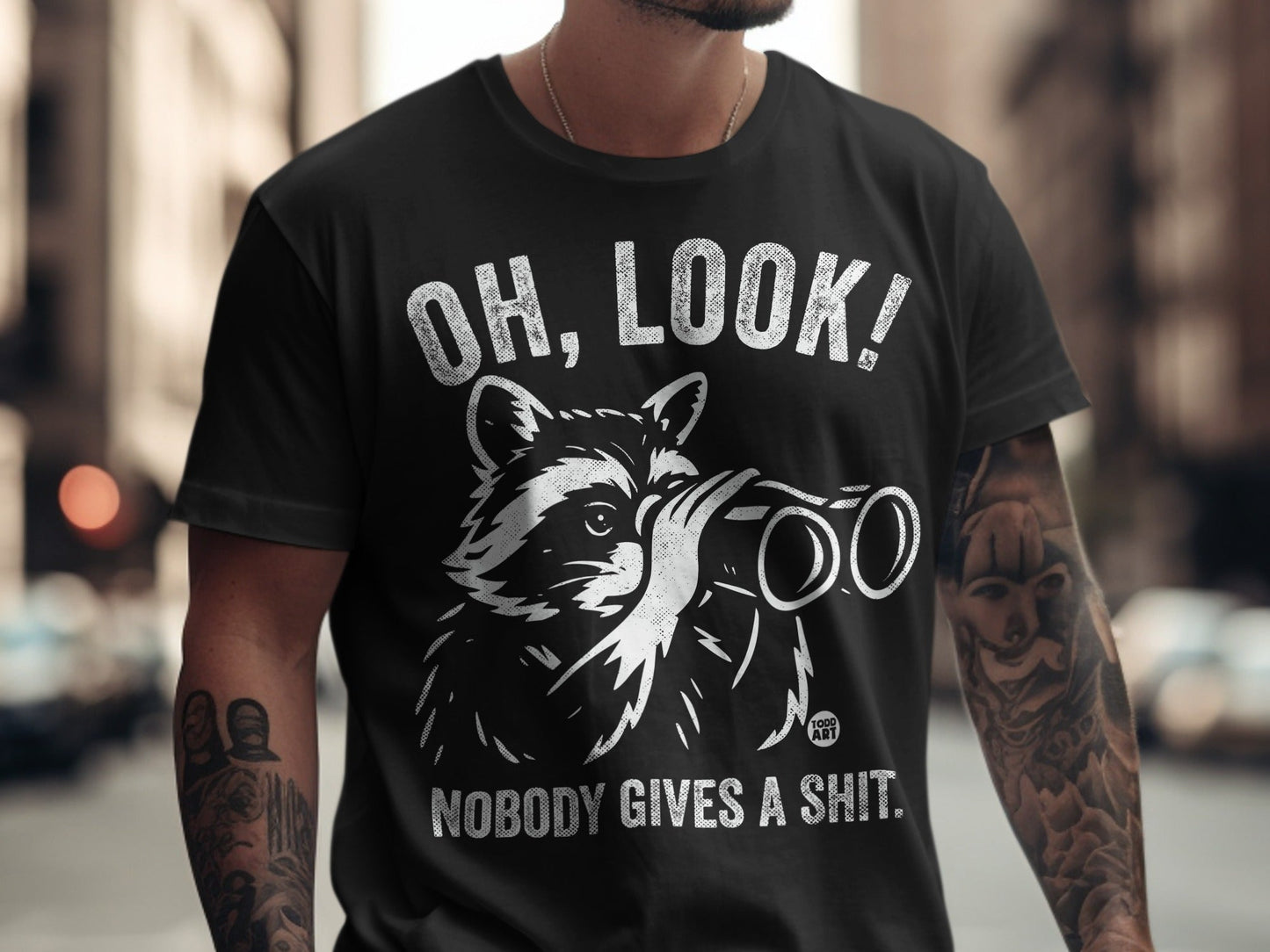 Black t-shirt with raccoon holding binoculars and text "OH, LOOK! NOBODY GIVES A SHIT."