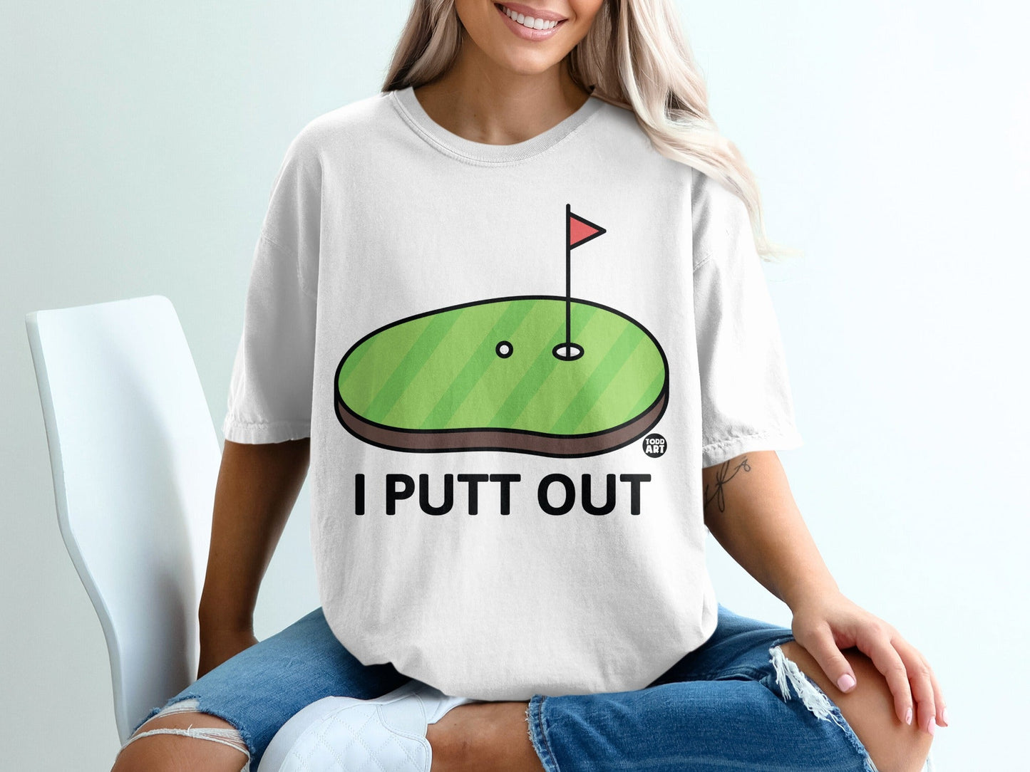 White t-shirt with "I PUTT OUT" and cartoon golf green with hole and flag.