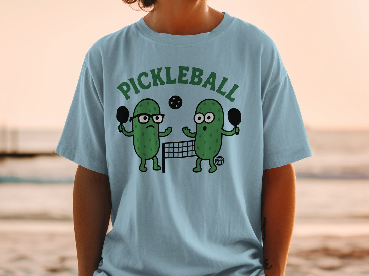 Two cartoon pickles playing pickleball on a beach.