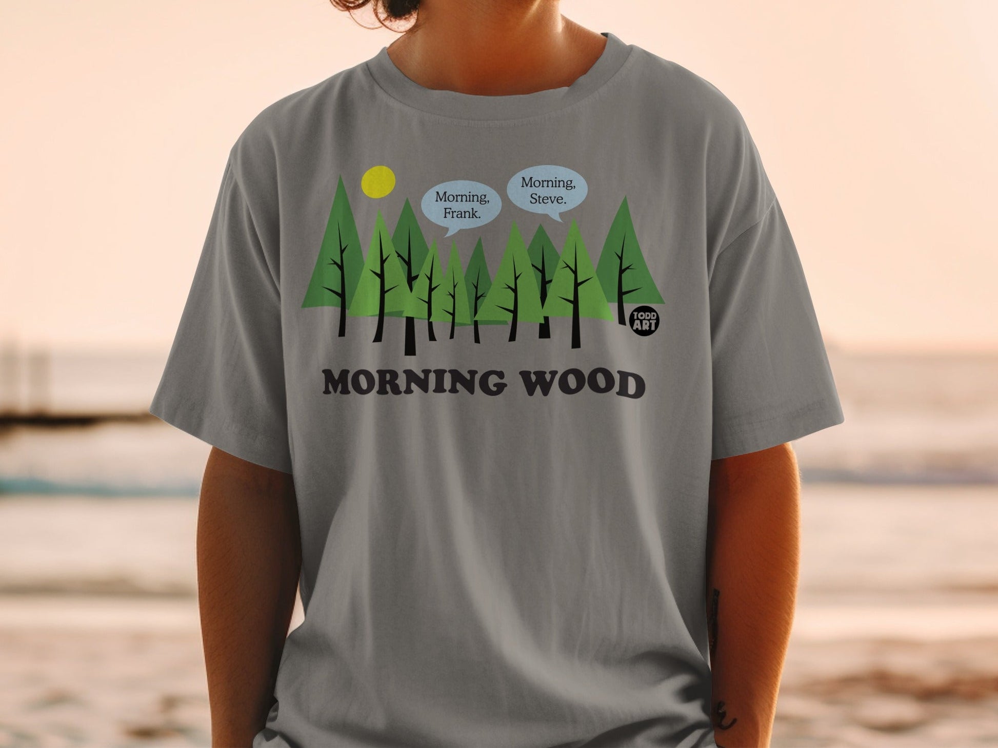 Gray t-shirt with trees, sun, and speech bubbles saying "Morning, Steve." and "Morning, Frank."