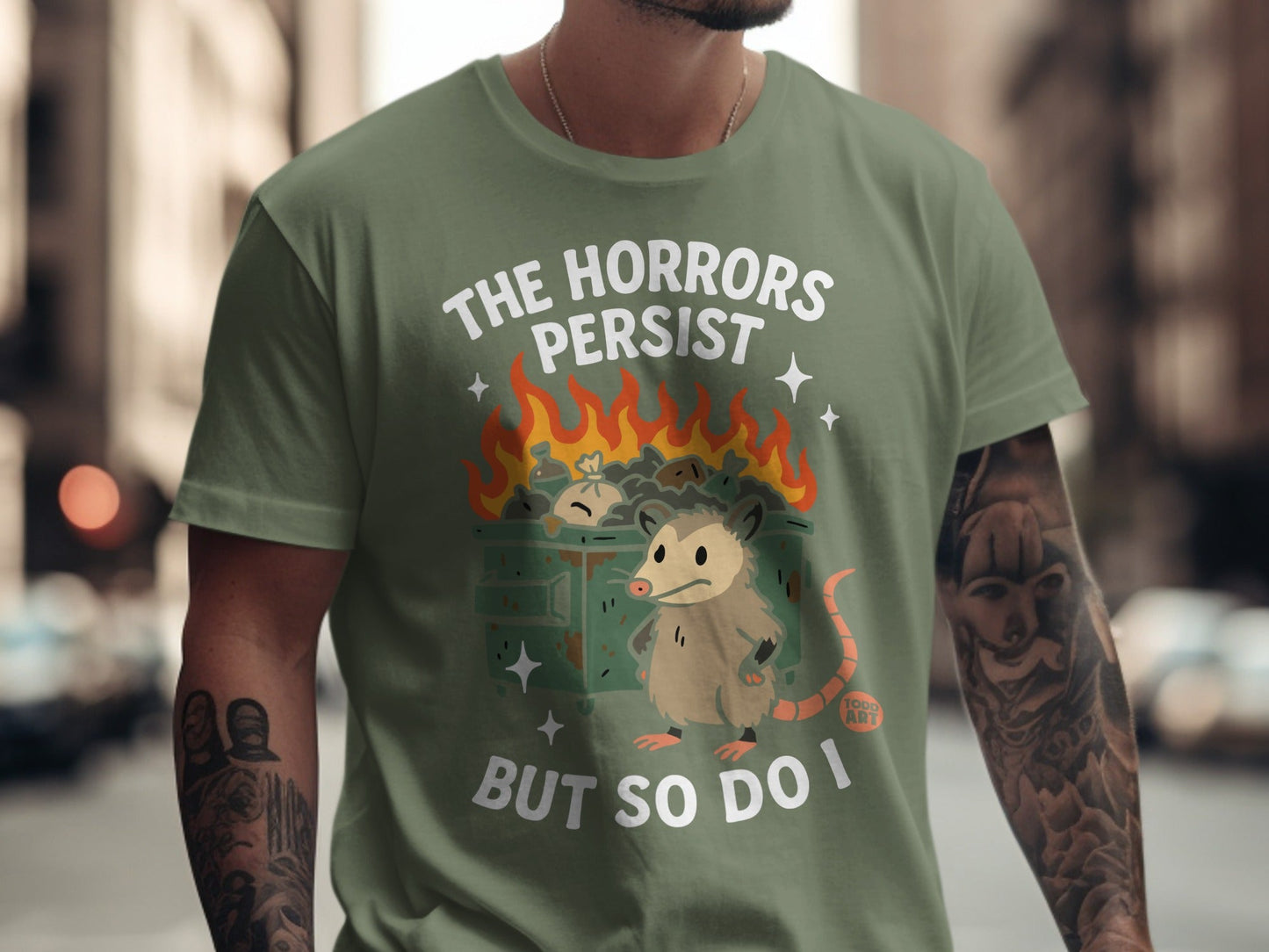 T-shirt with possum in burning dumpster, text "The horrors persist but so do I".