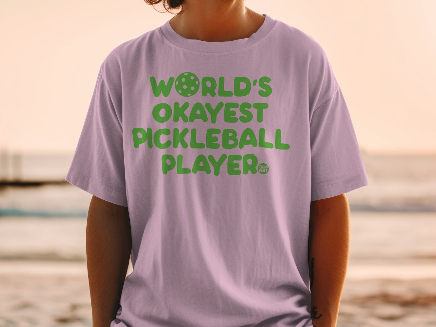 Purple t-shirt with "WORLD'S OKAYEST PICKLEBALL PLAYER" in green text.