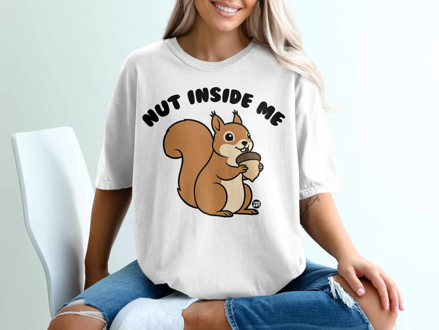 White t-shirt with graphic of a cartoon squirrel holding an acorn and text "NUT INSIDE ME".
