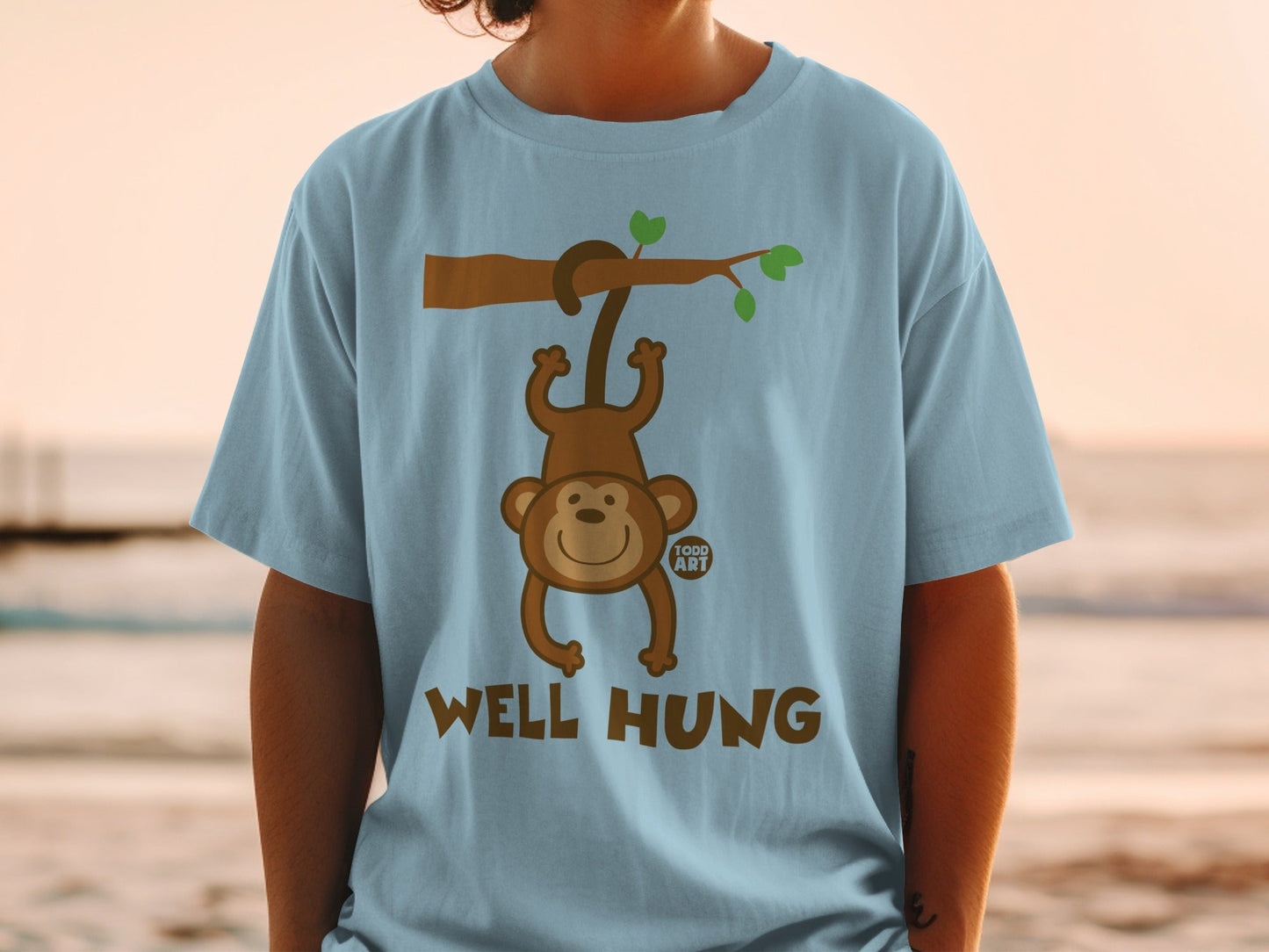 Light blue t-shirt with cartoon monkey hanging from tree branch, text "WELL HUNG".