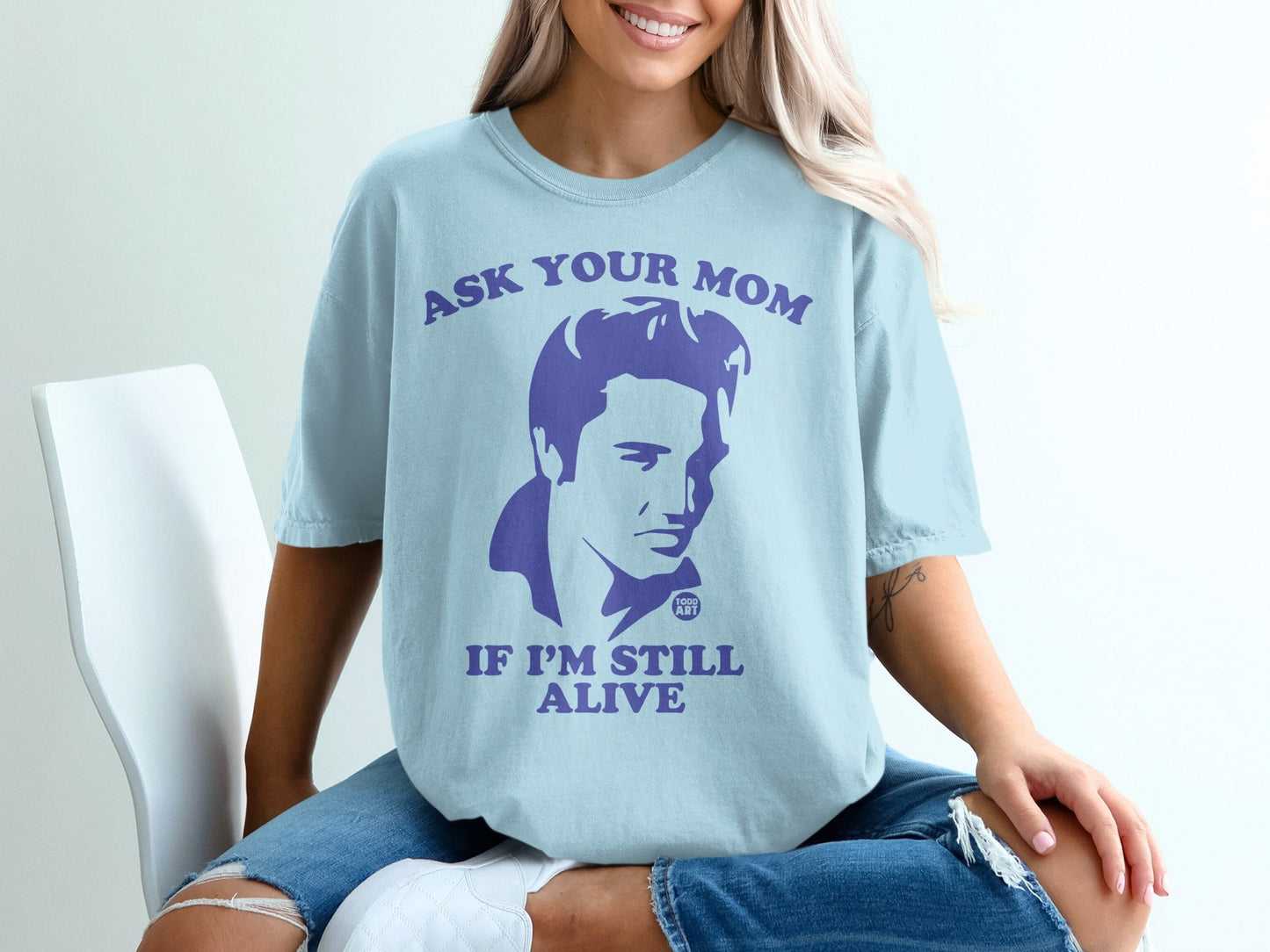 Light blue t-shirt with a purple graphic of Elvis Presley and the text "Ask Your Mom If I'm Still Alive".