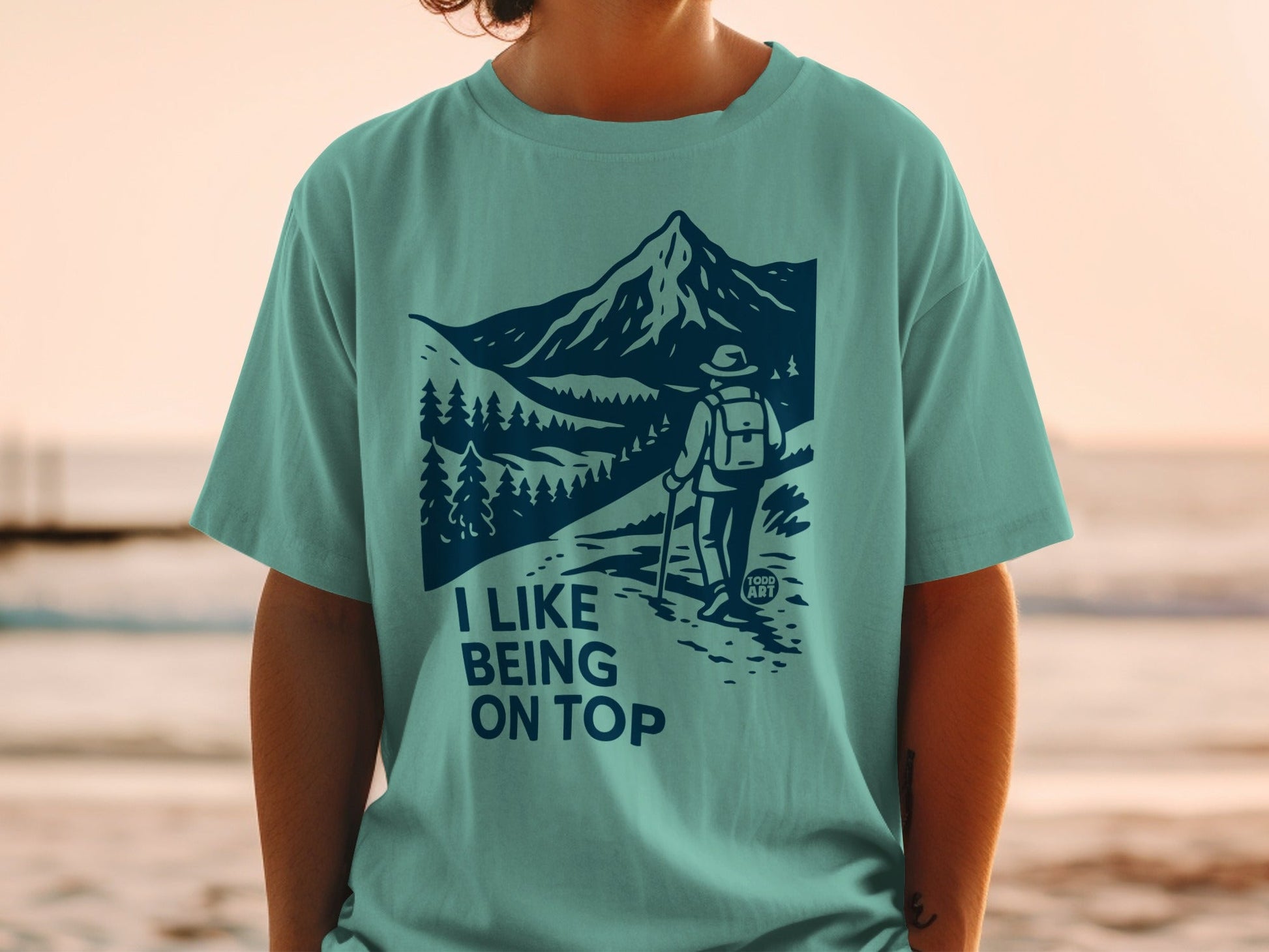 Teal t-shirt with graphic of hiker on mountain path, "I like being on top" text.