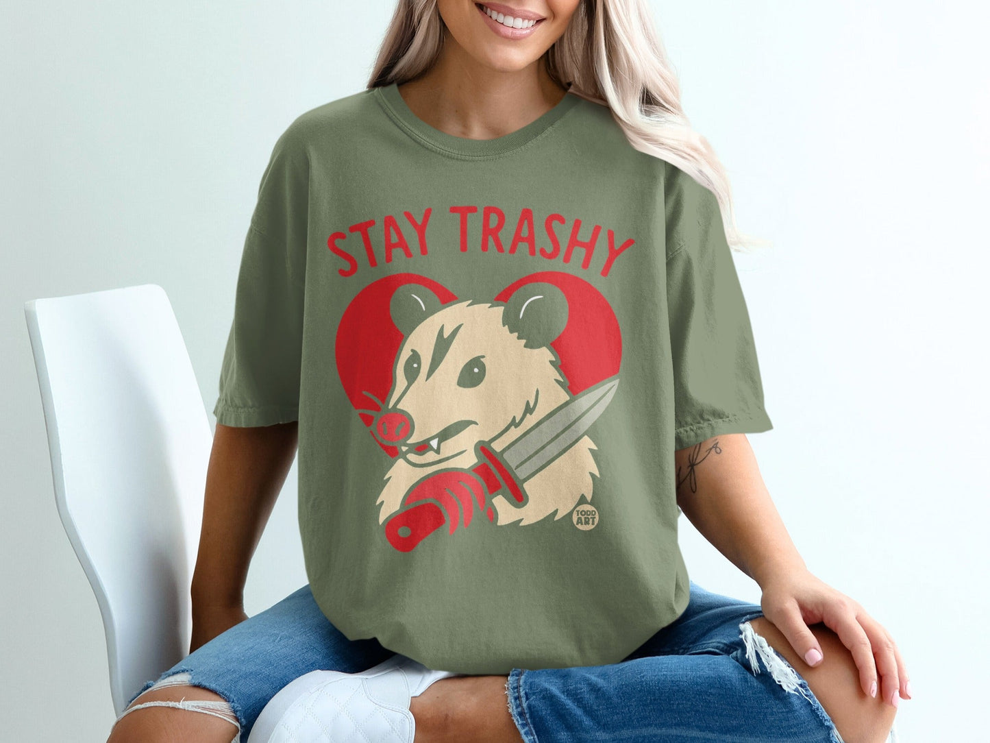 Opossum wearing shirt that says "STAY TRASHY" holding a knife.
