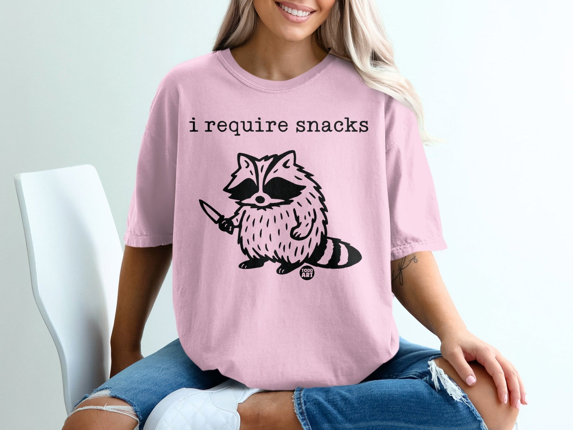 T-shirt with raccoon graphic and text "i require snacks"