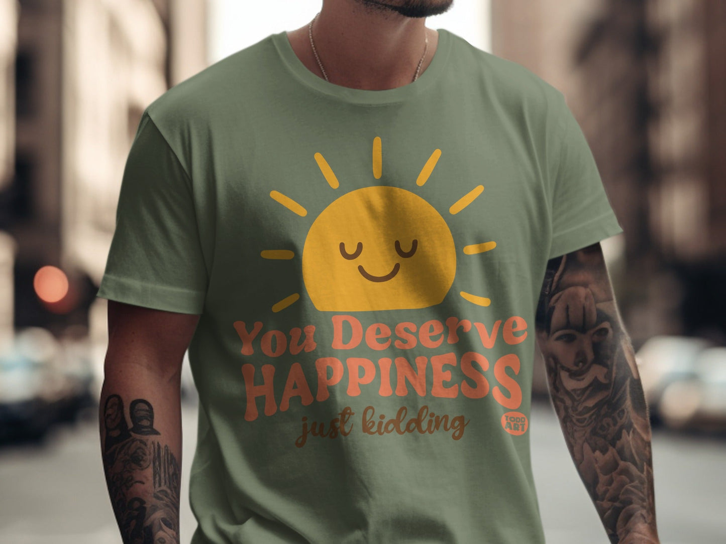Green t-shirt with "You Deserve Happiness" and "just kidding" text and sun graphic.