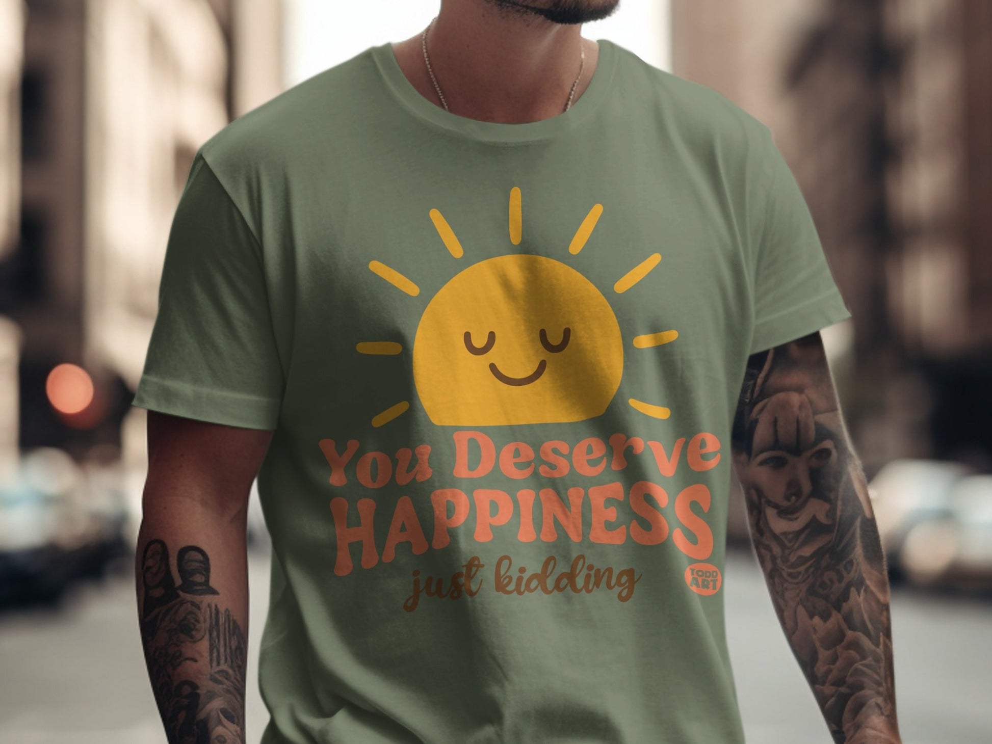 Green t-shirt with "You Deserve Happiness" and "just kidding" text and sun graphic.