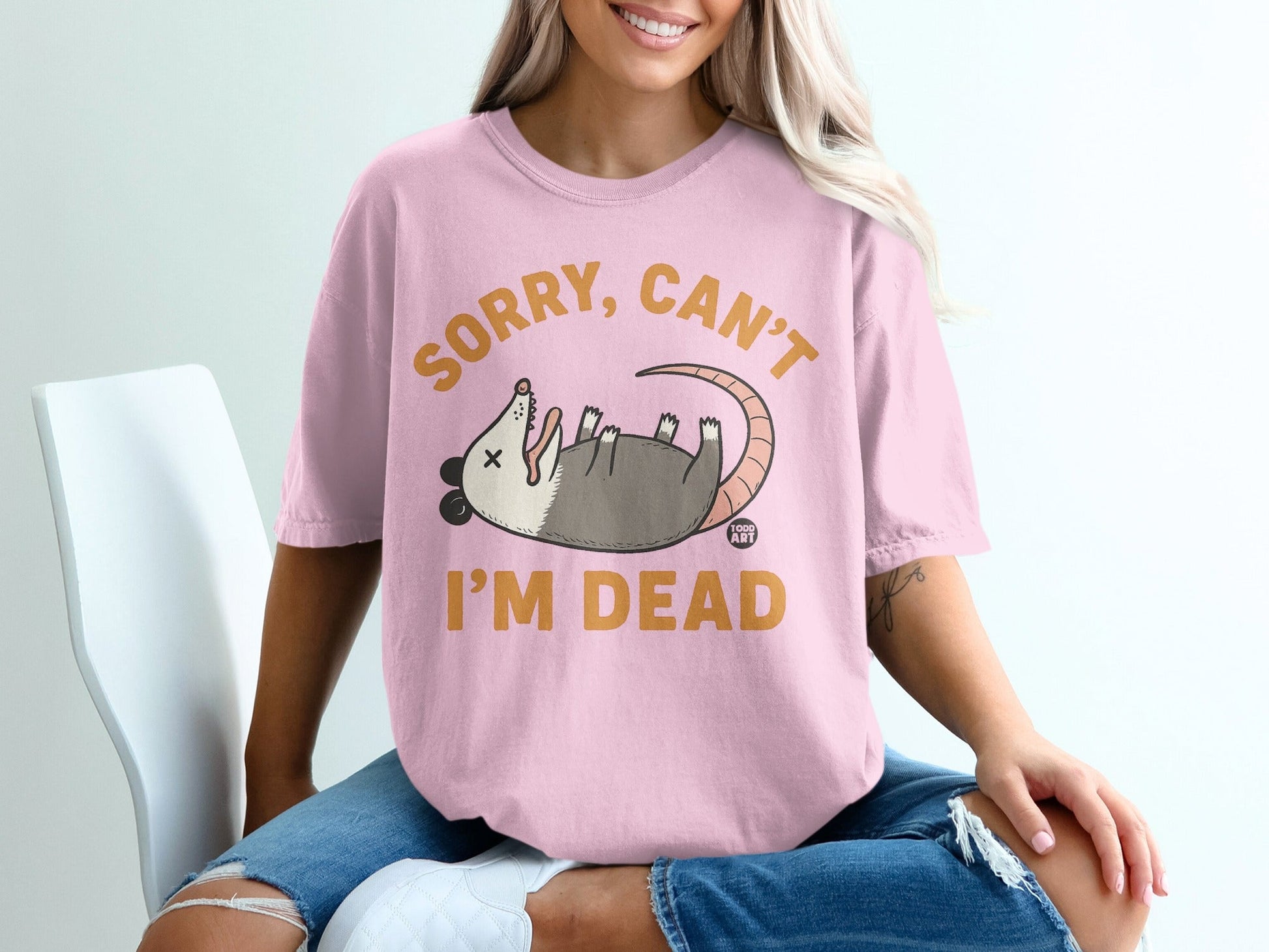 Pink t-shirt with a cartoon opossum and text "SORRY, CAN'T I'M DEAD".