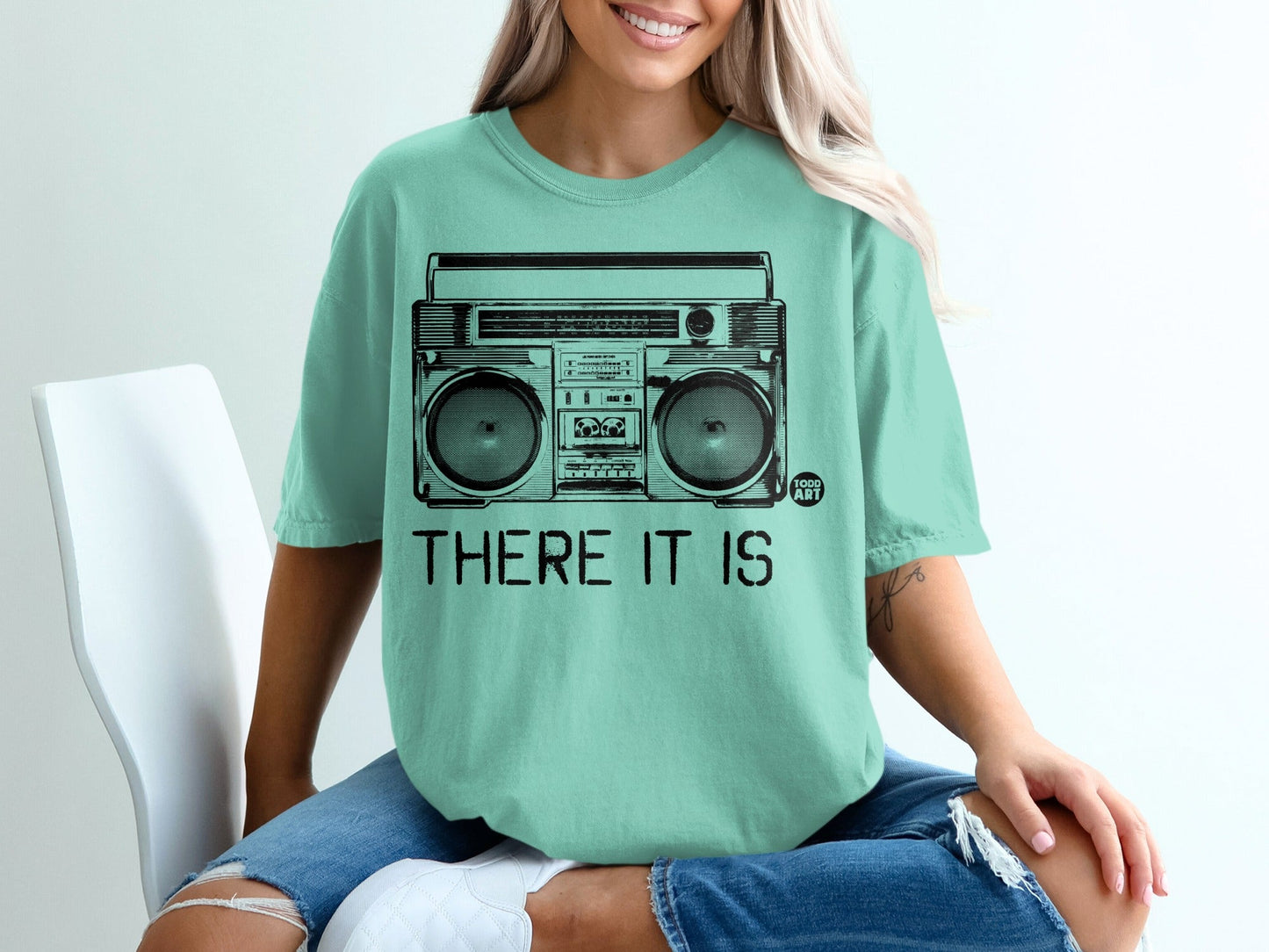 Teal t-shirt with black line art of a boombox and text "THERE IT IS".