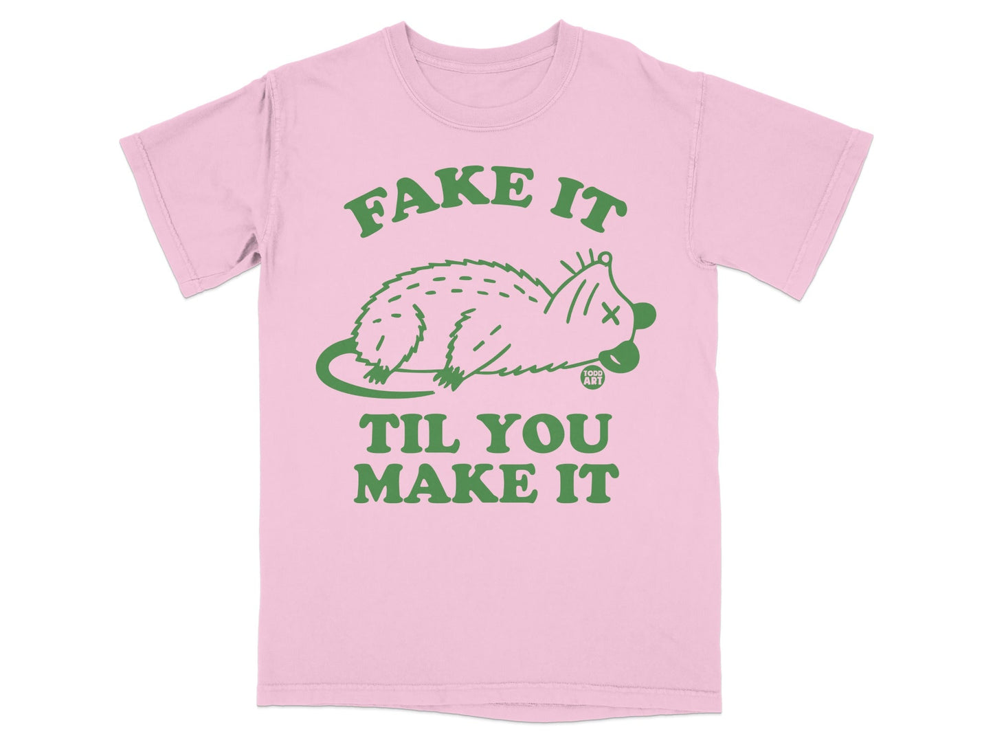 Pink t-shirt with green text and a drawing of a possum saying "Fake It Til You Make It".