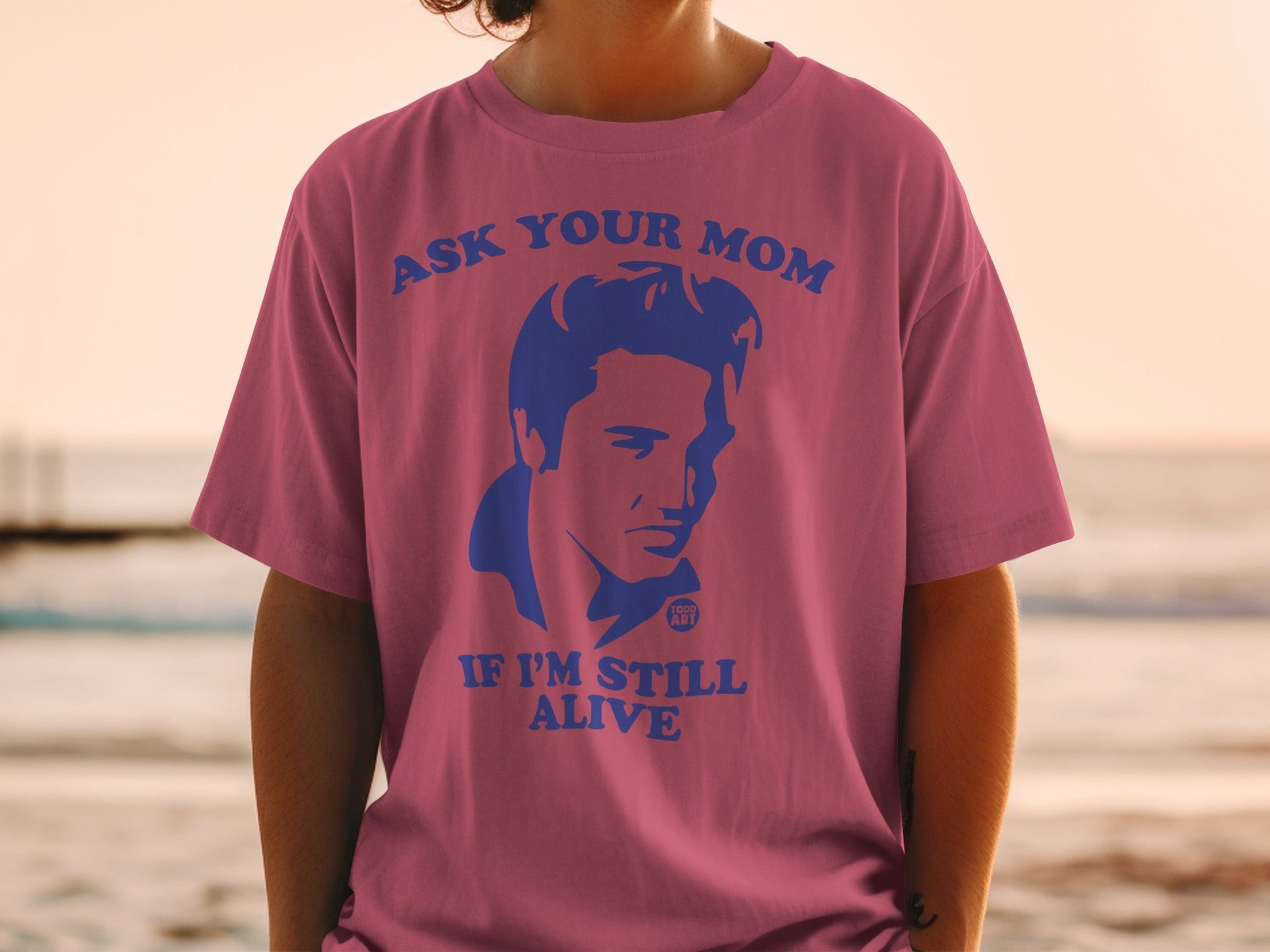 Pink t-shirt with blue graphic of Elvis Presley and text "ASK YOUR MOM IF I'M STILL ALIVE".