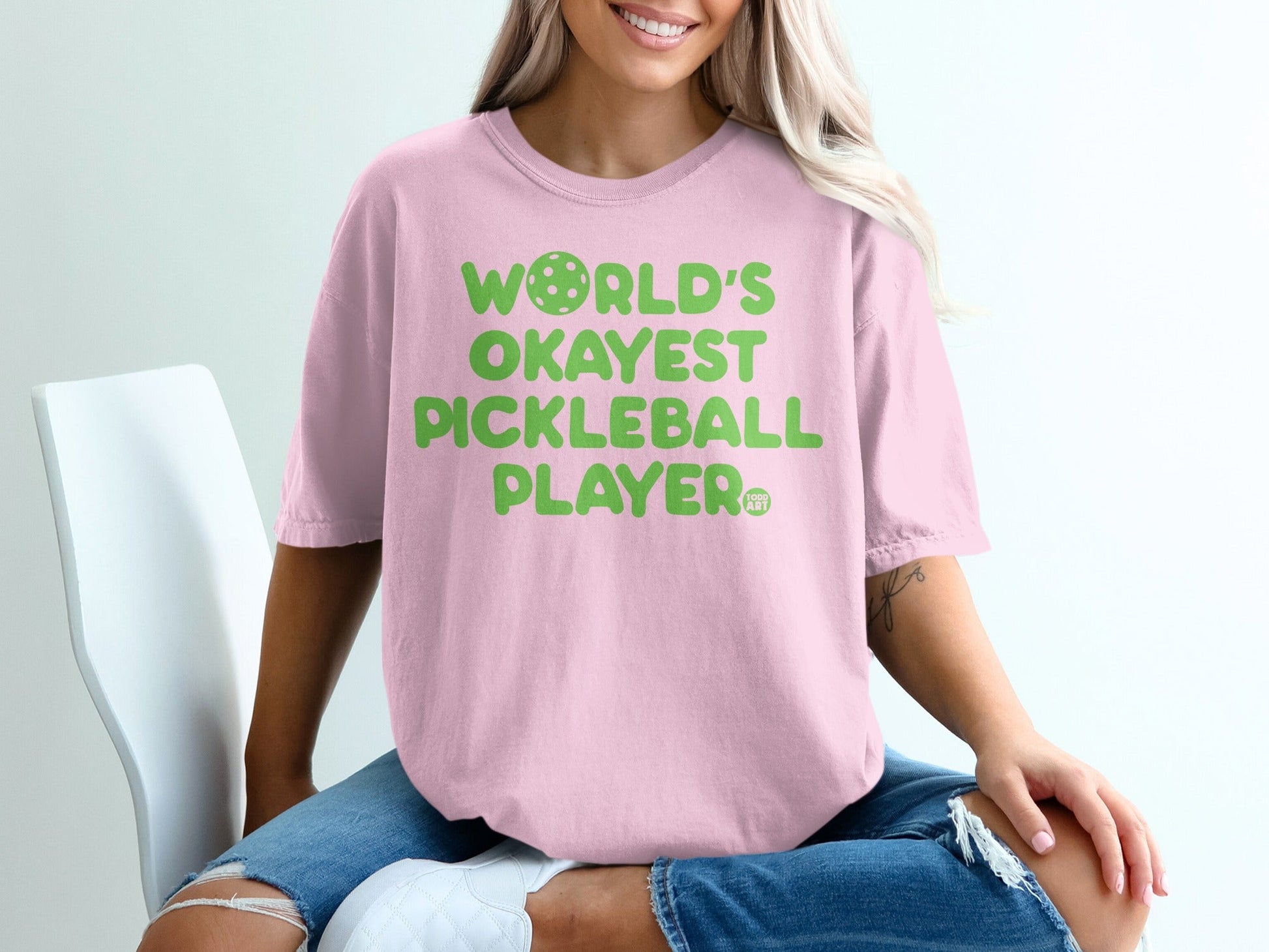 Pink t-shirt with "World's Okayest Pickleball Player" text and pickleball graphic.
