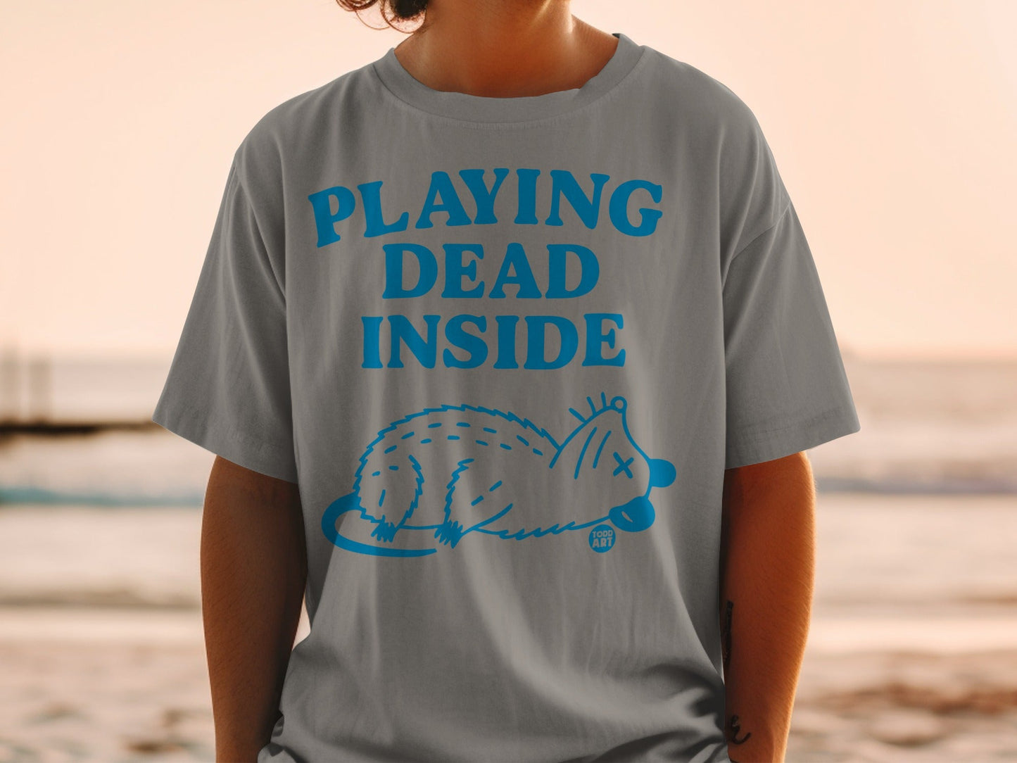 Grey t-shirt with blue text "PLAYING DEAD INSIDE" and a cartoon opossum.