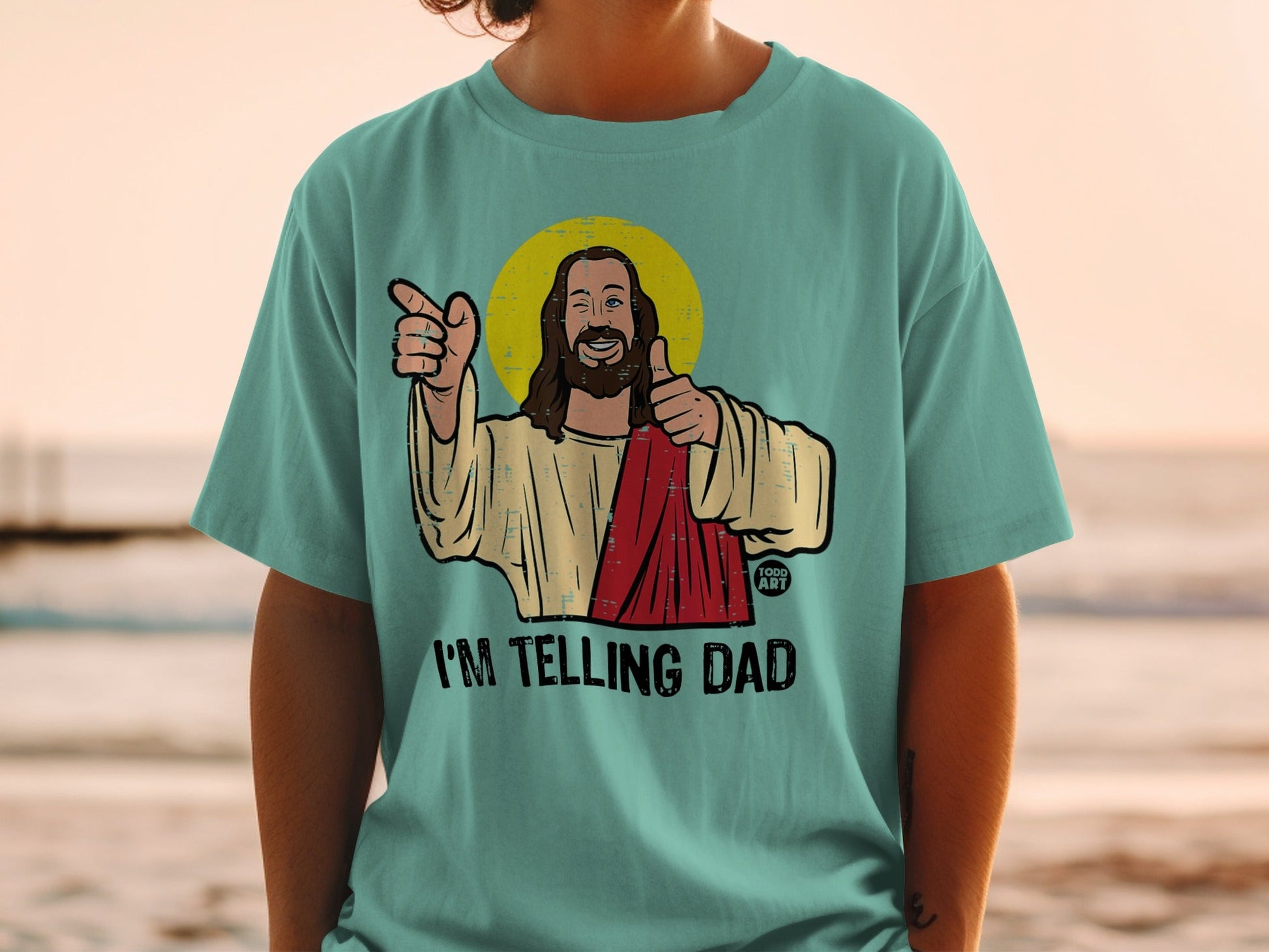 Teal t-shirt with cartoon Jesus giving a thumbs up and pointing.