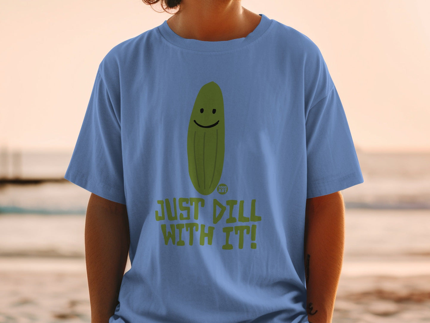 Blue t-shirt with a smiling pickle illustration and text that reads "JUST DILL WITH IT!".