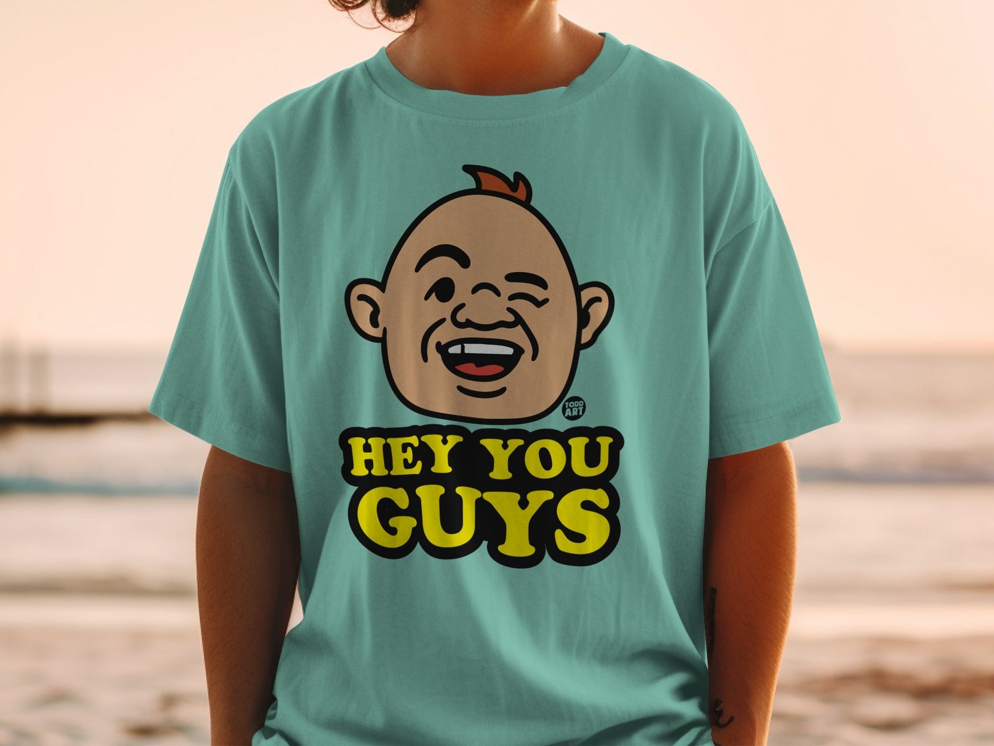 Teal t-shirt with cartoon character winking and text "HEY YOU GUYS".