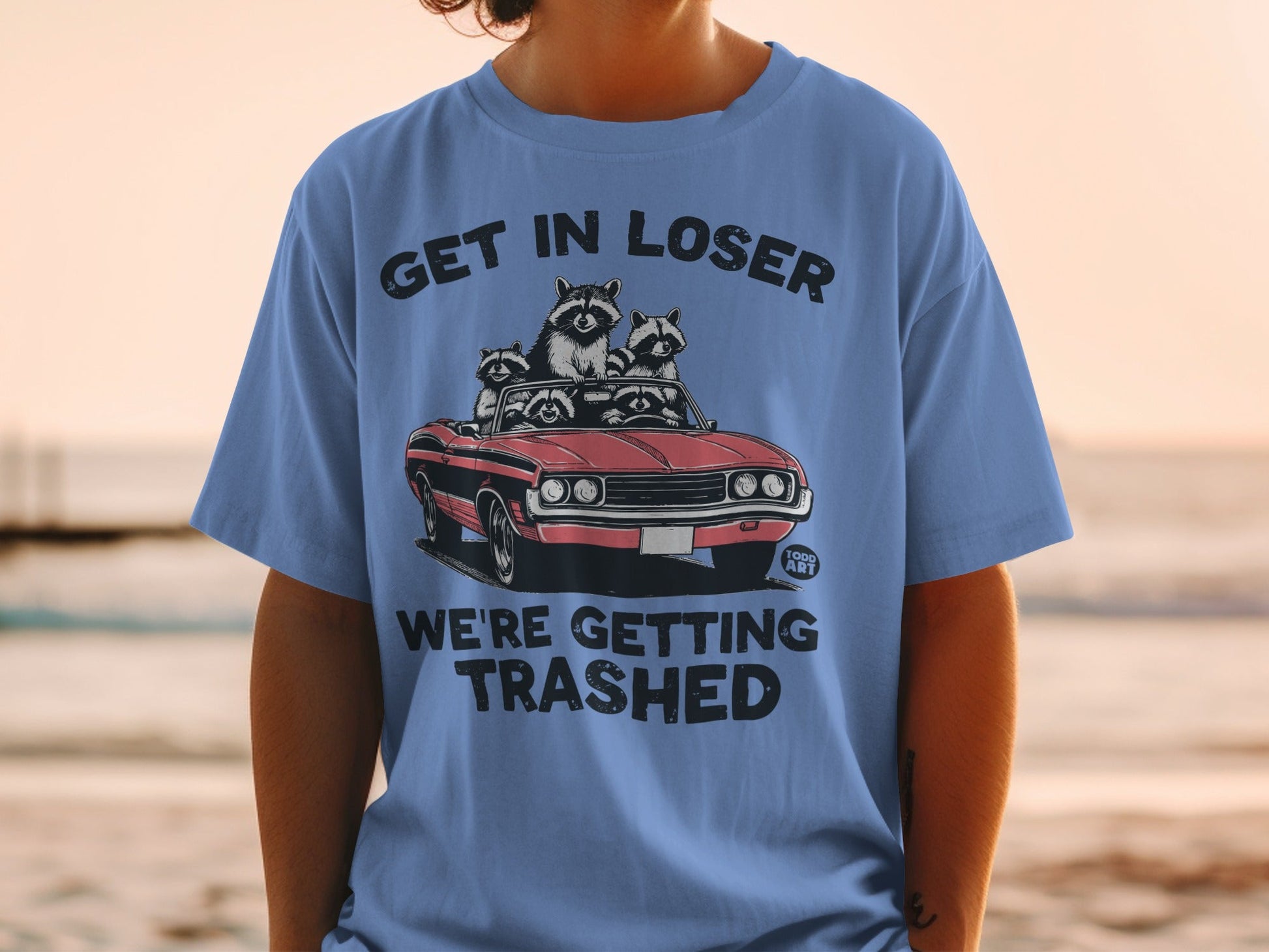 Blue t-shirt with raccoons in a convertible, text reads "Get in loser, we're getting trashed."