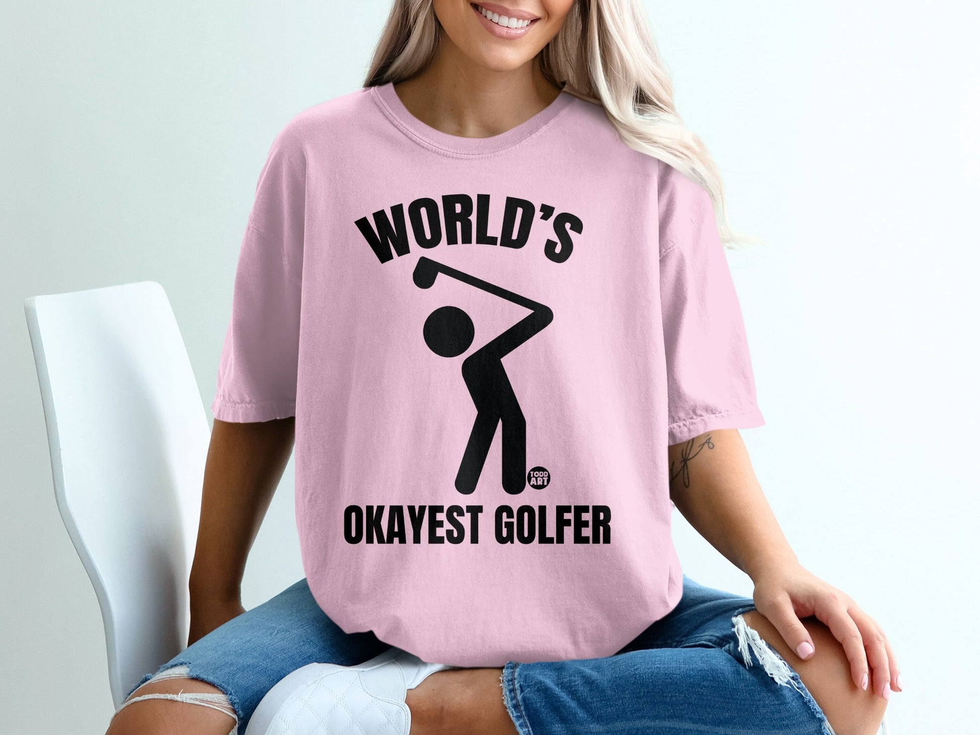 Pink t-shirt with "World's Okayest Golfer" text and a golfer silhouette.