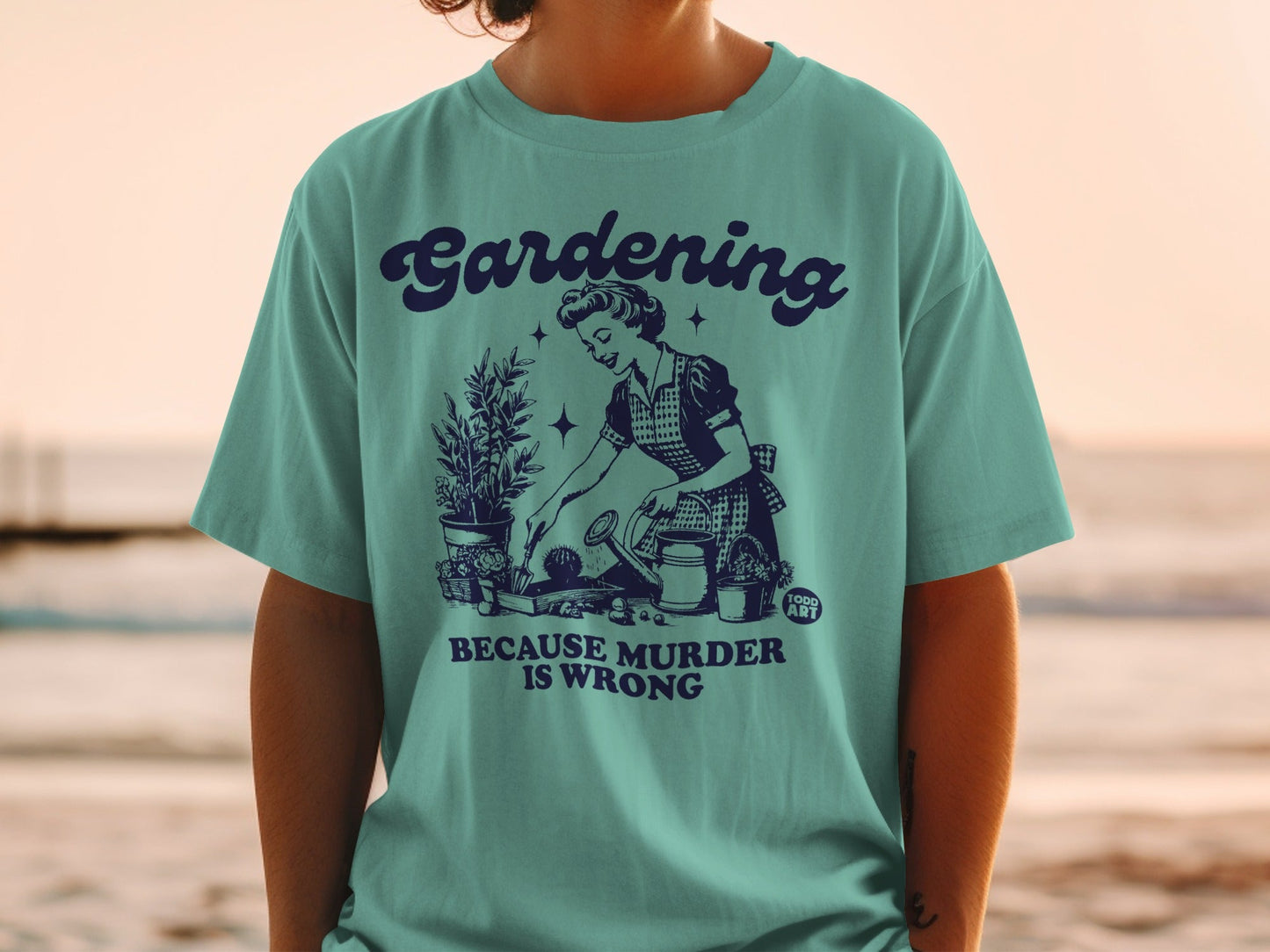 Teal t-shirt with vintage graphic of woman gardening and text "Gardening is murder because wrong."
