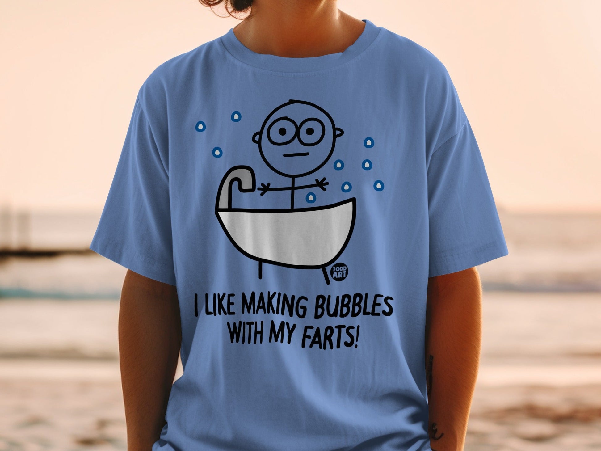 Blue t-shirt with cartoon figure in a bathtub saying "I like making bubbles with my farts!"