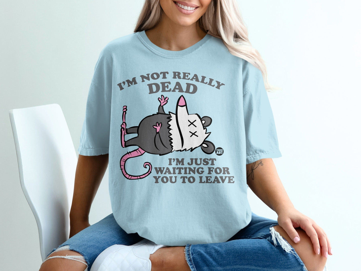 Light blue t-shirt with a cartoon opossum saying "I'm not really dead, I'm just waiting for you to leave."