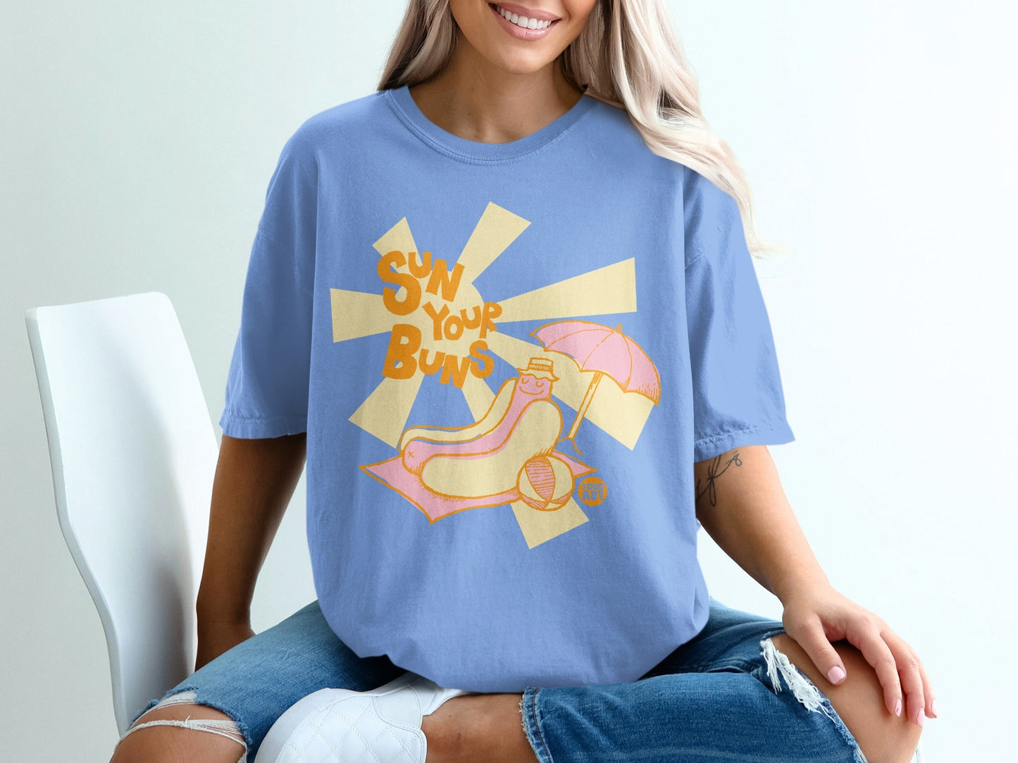Blue t-shirt with a cartoon hot dog sunbathing under an umbrella.