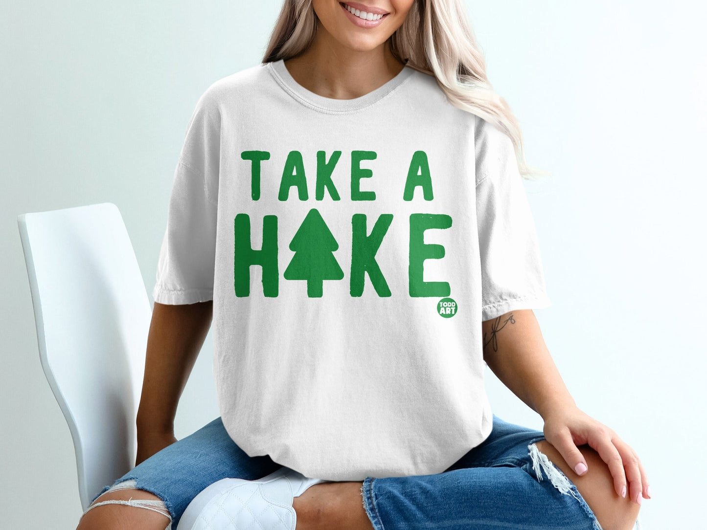 White t-shirt with green text and tree graphic saying "TAKE A HIKE".