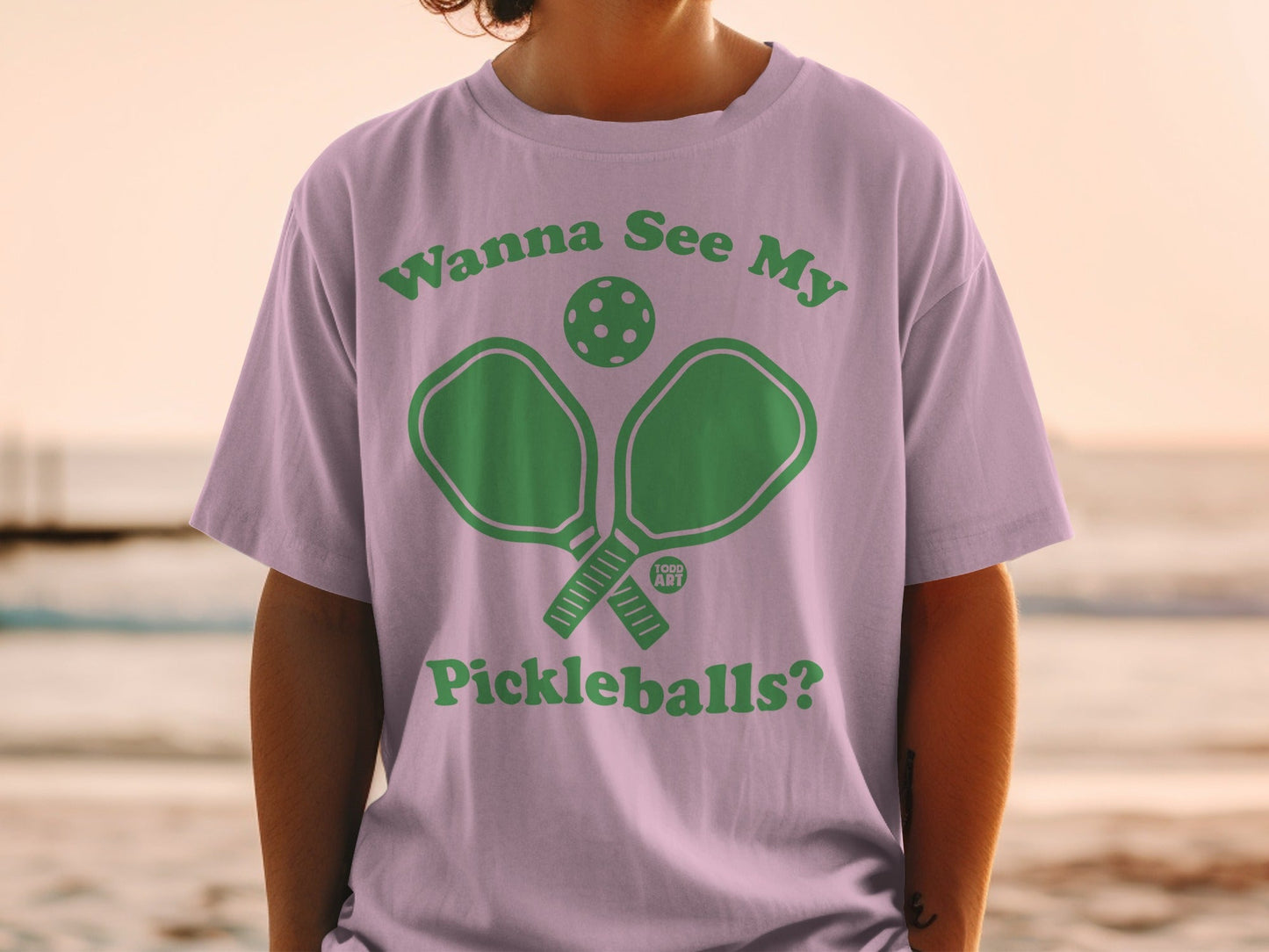 Green pickleball paddles and ball graphic on a purple t-shirt.