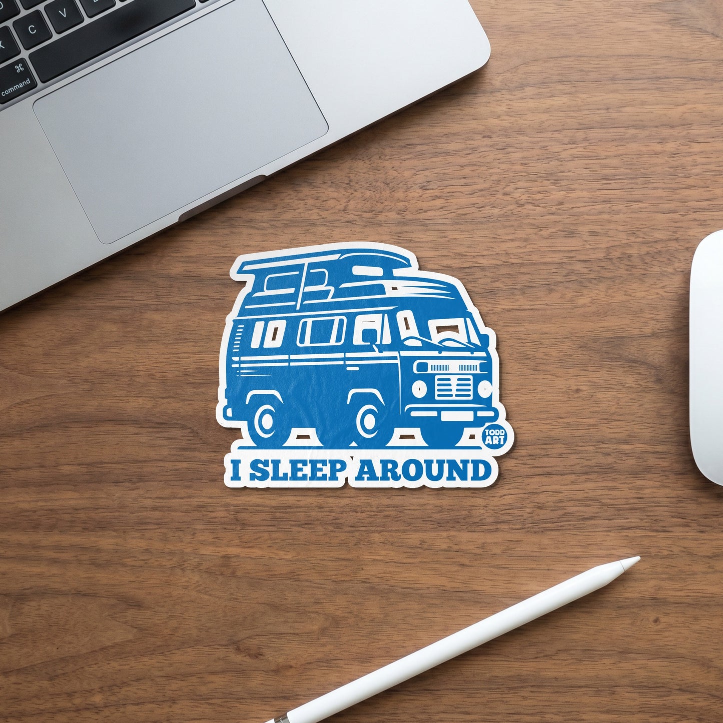 Blue camper van sticker with text "I SLEEP AROUND" on wooden desk.