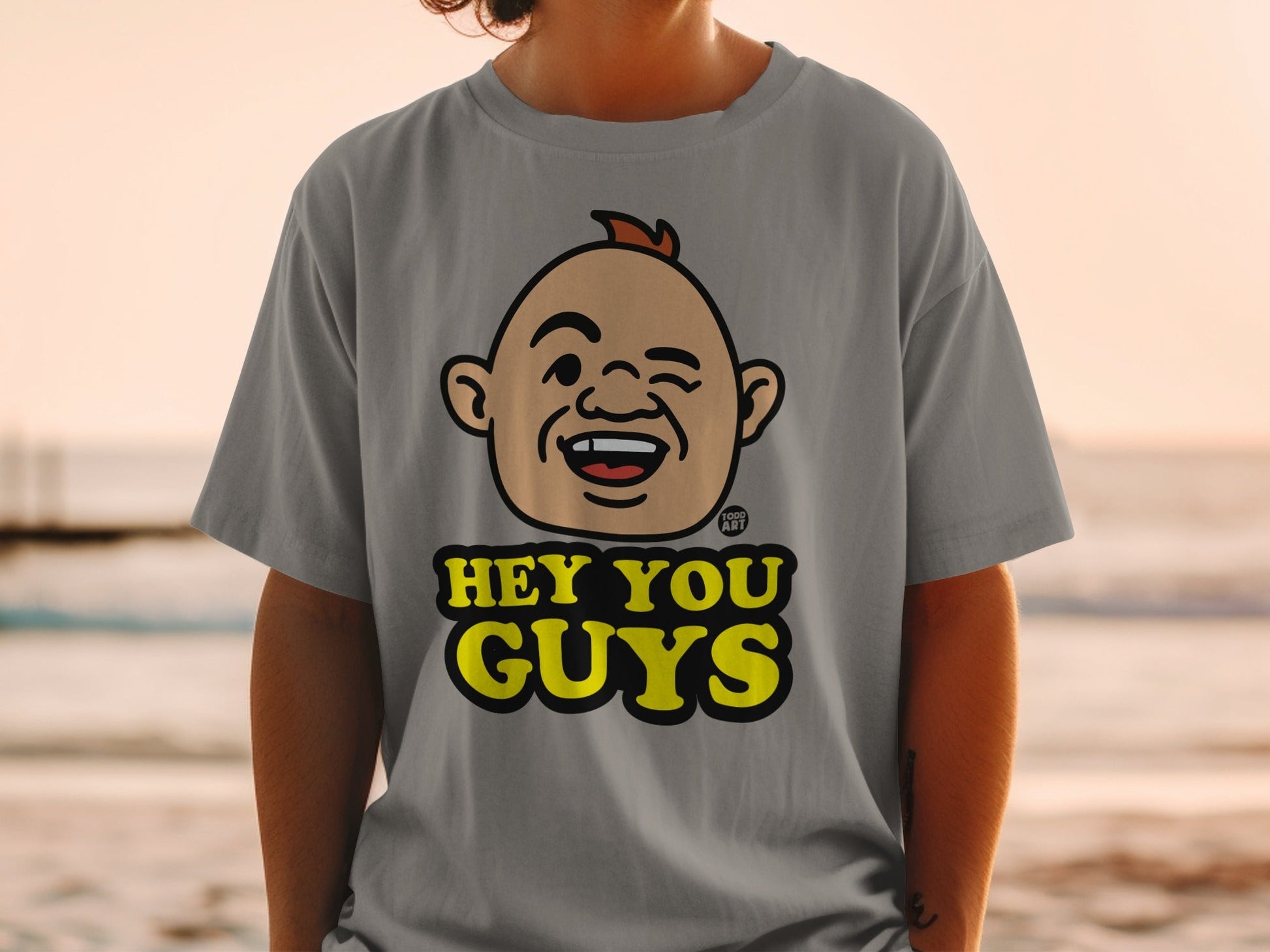 Grey t-shirt with a cartoon face and "Hey You Guys" text.