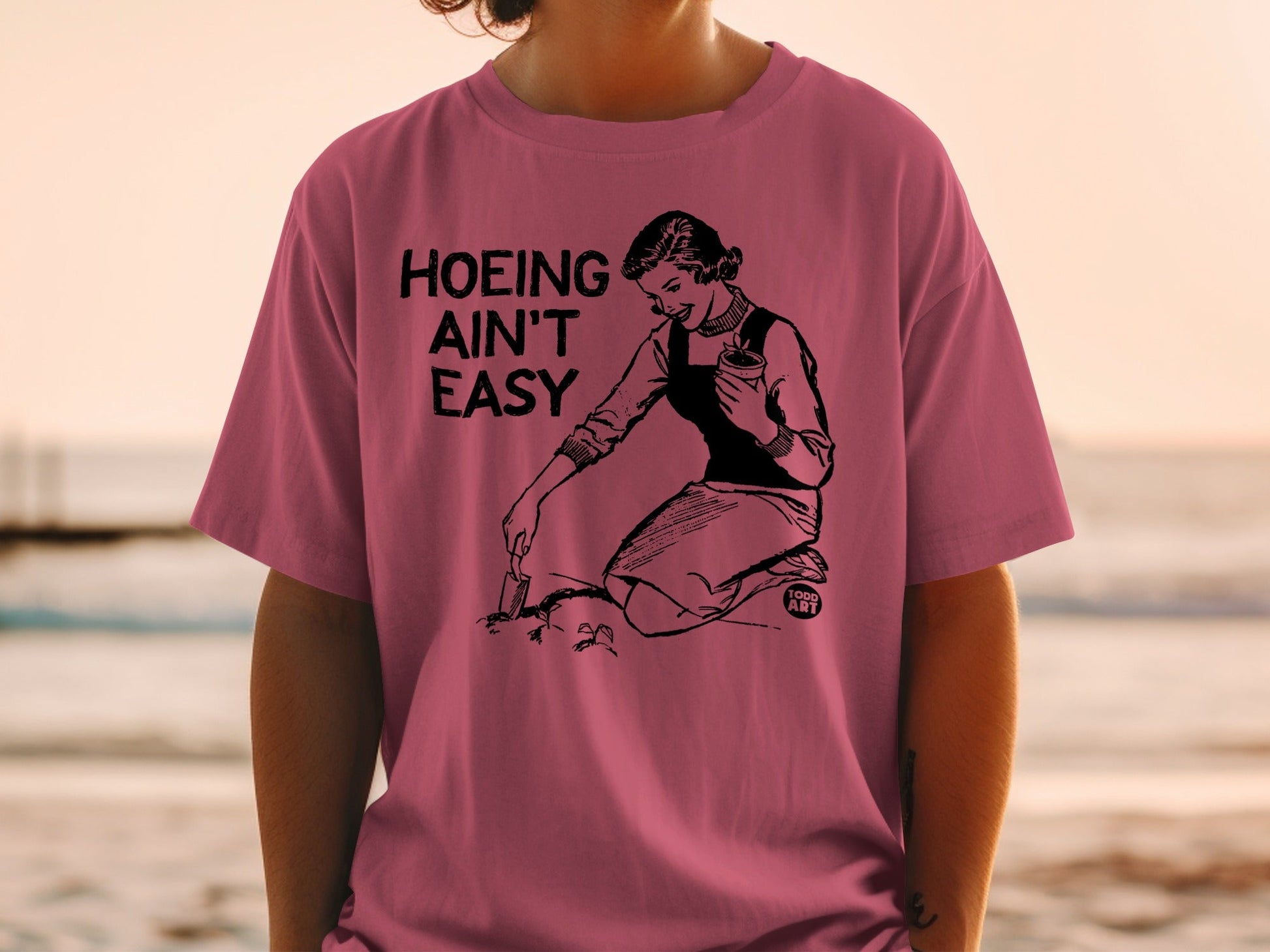 T-shirt with "Hoeing Ain't Easy" graphic of a woman gardening at the beach.