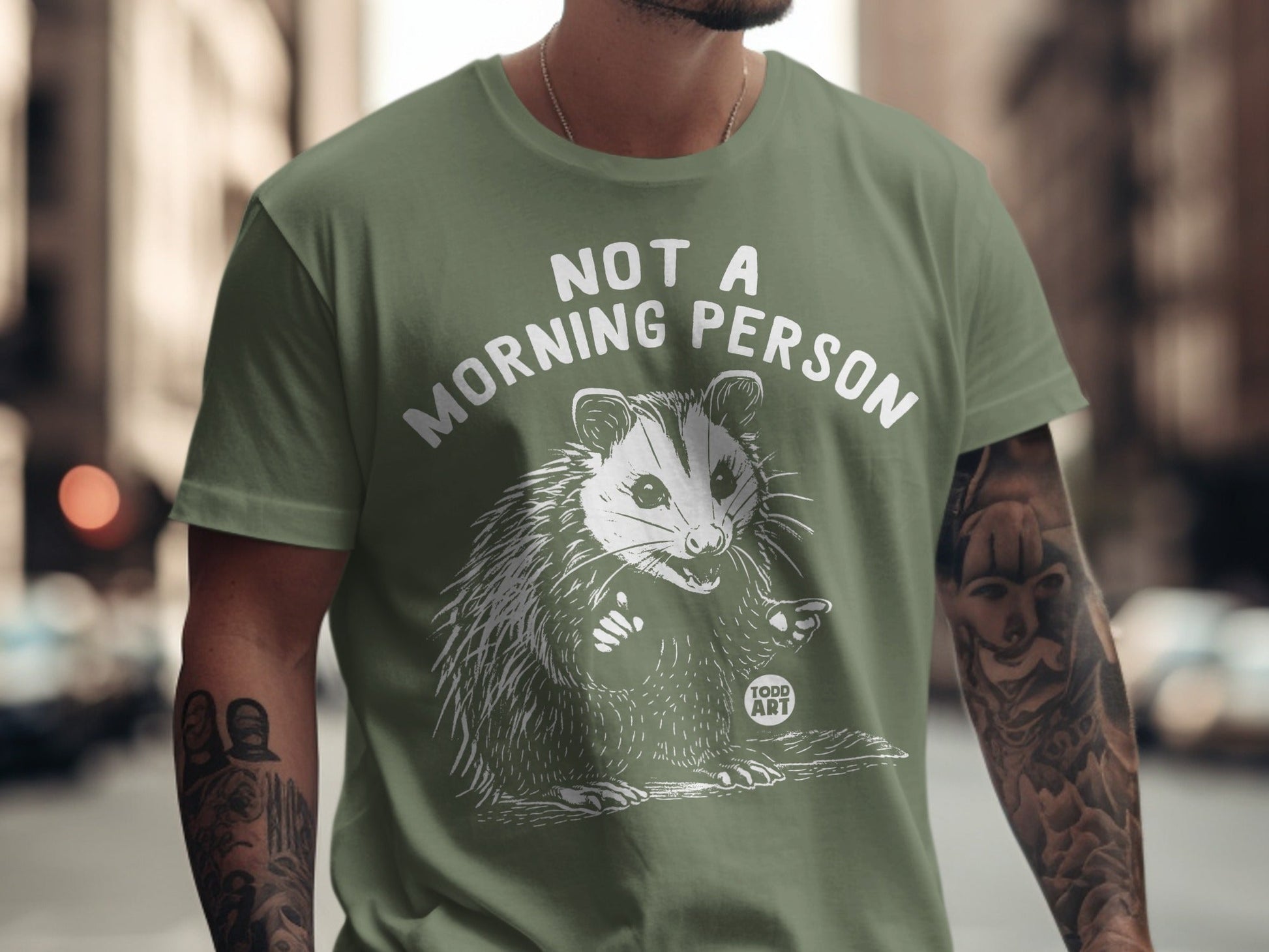 Green t-shirt with white text "NOT A MORNING PERSON" and an opossum graphic.