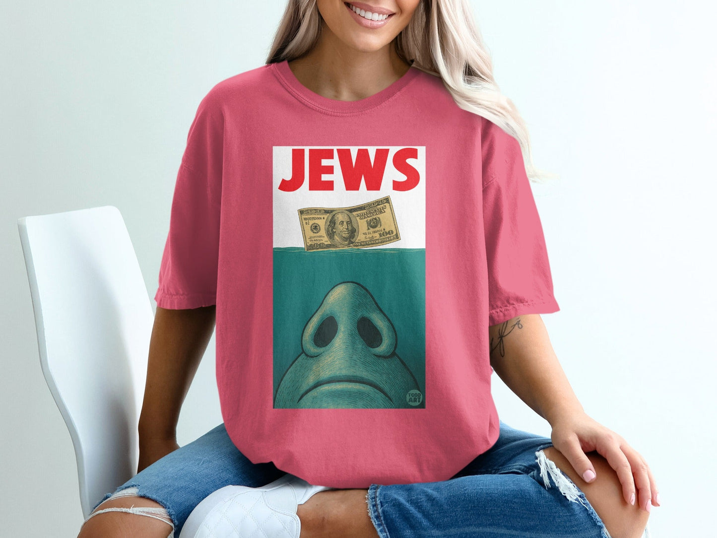 Pink t-shirt with "JEWS" text above a blue nose and a dollar bill.