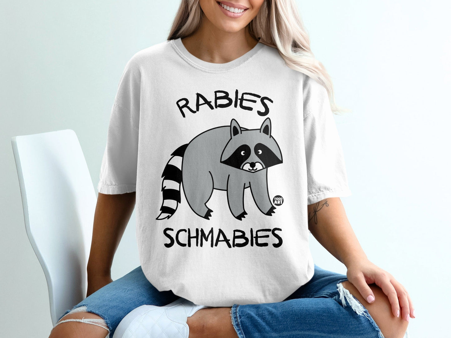 White t-shirt with cartoon raccoon and text "Rabies Schmabies".