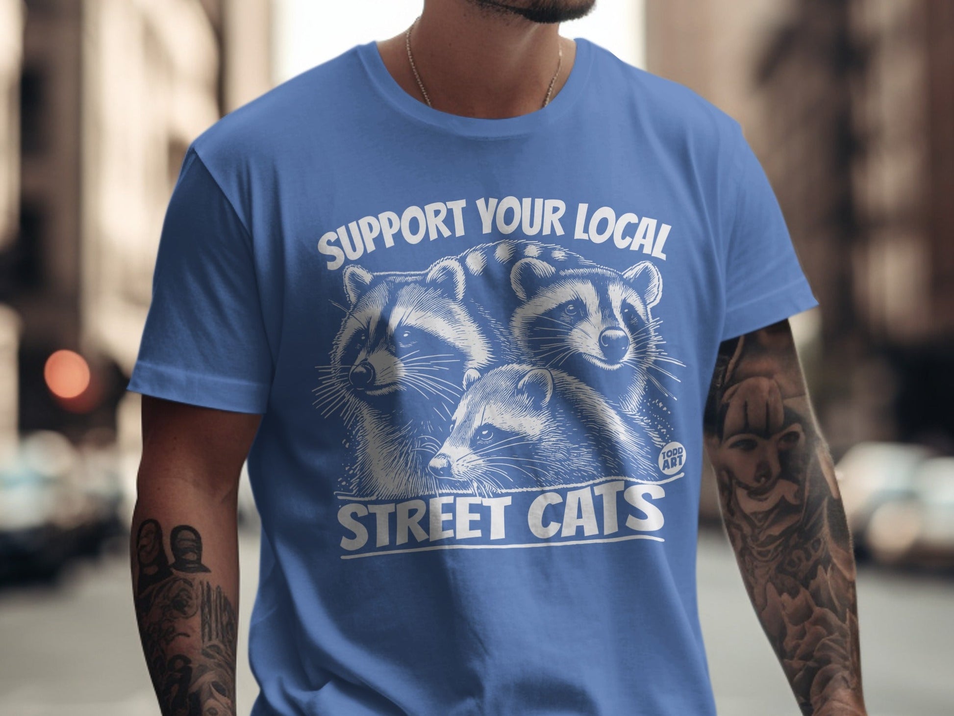 Blue t-shirt with "SUPPORT YOUR LOCAL STREET CATS" and raccoon graphic.